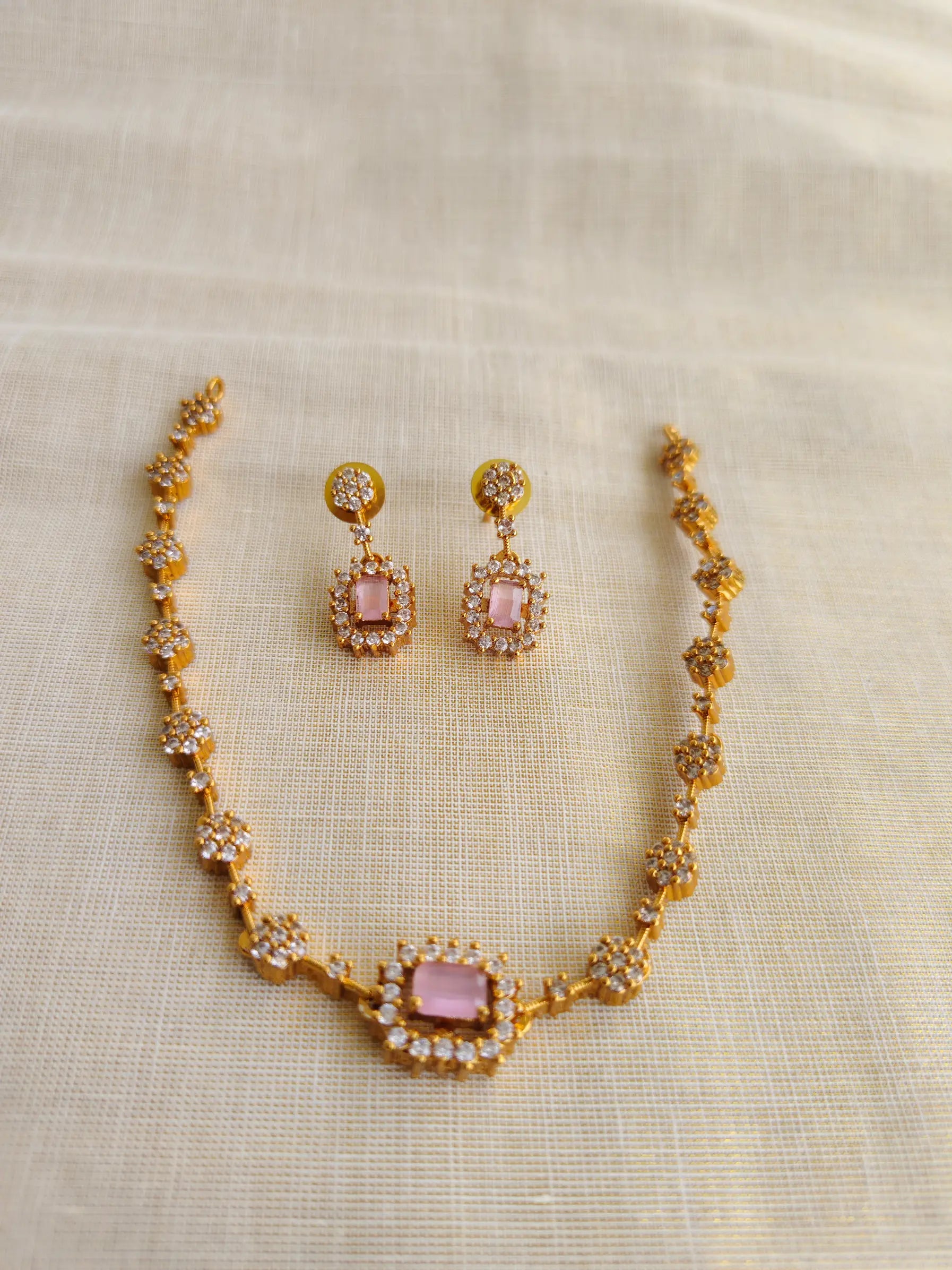 Gold necklace and earrings with pink stones on a beige fabric background