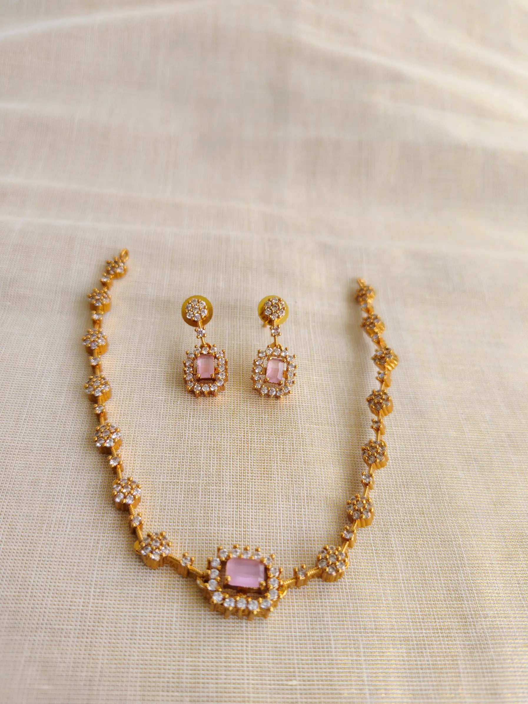 Gold necklace and earrings with pink stones on a beige fabric background