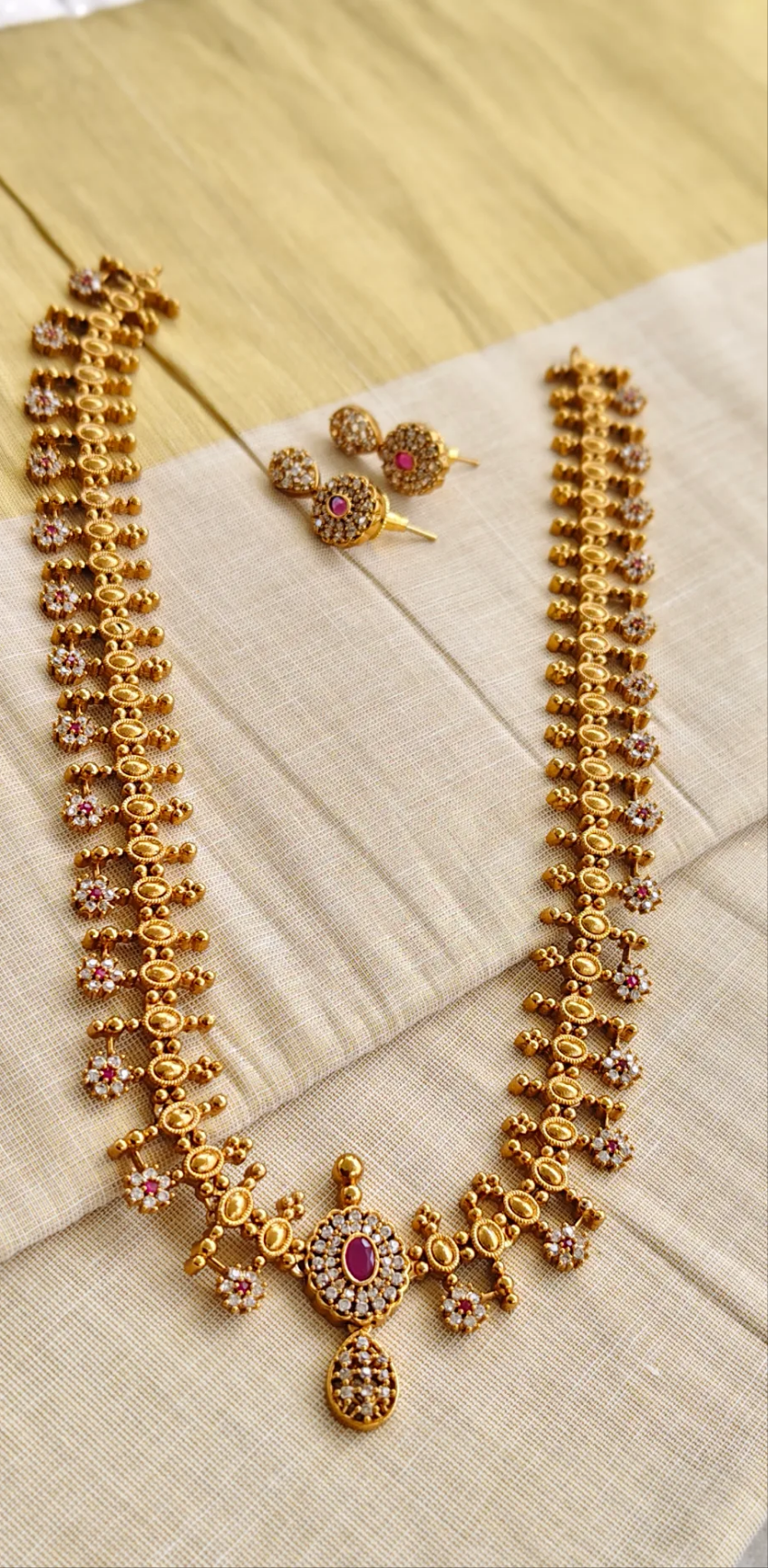 Gold necklace with ruby red stones and matching earrings on a beige fabric background