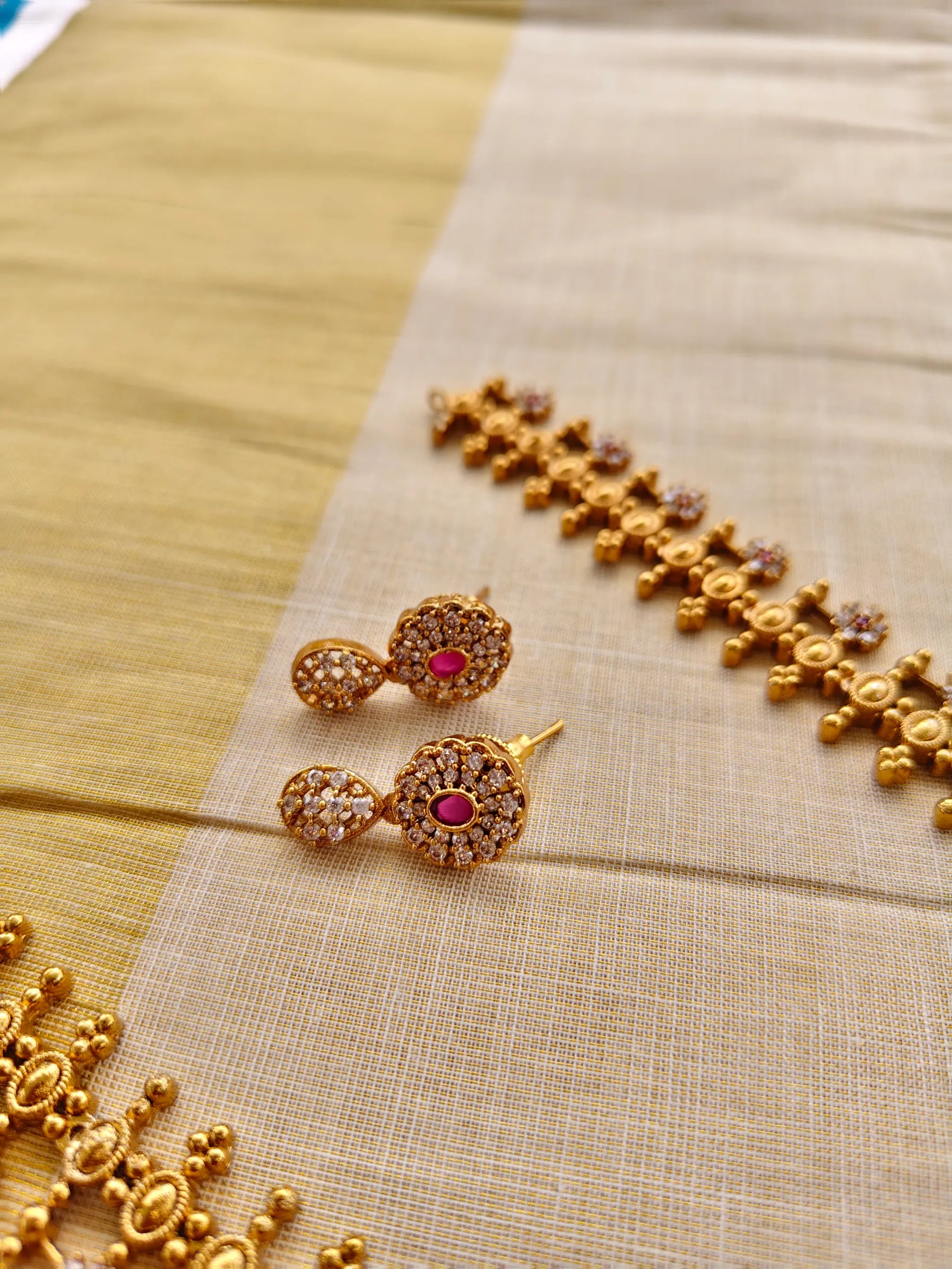 Gold earrings with ruby red gemstones on a beige fabric background
