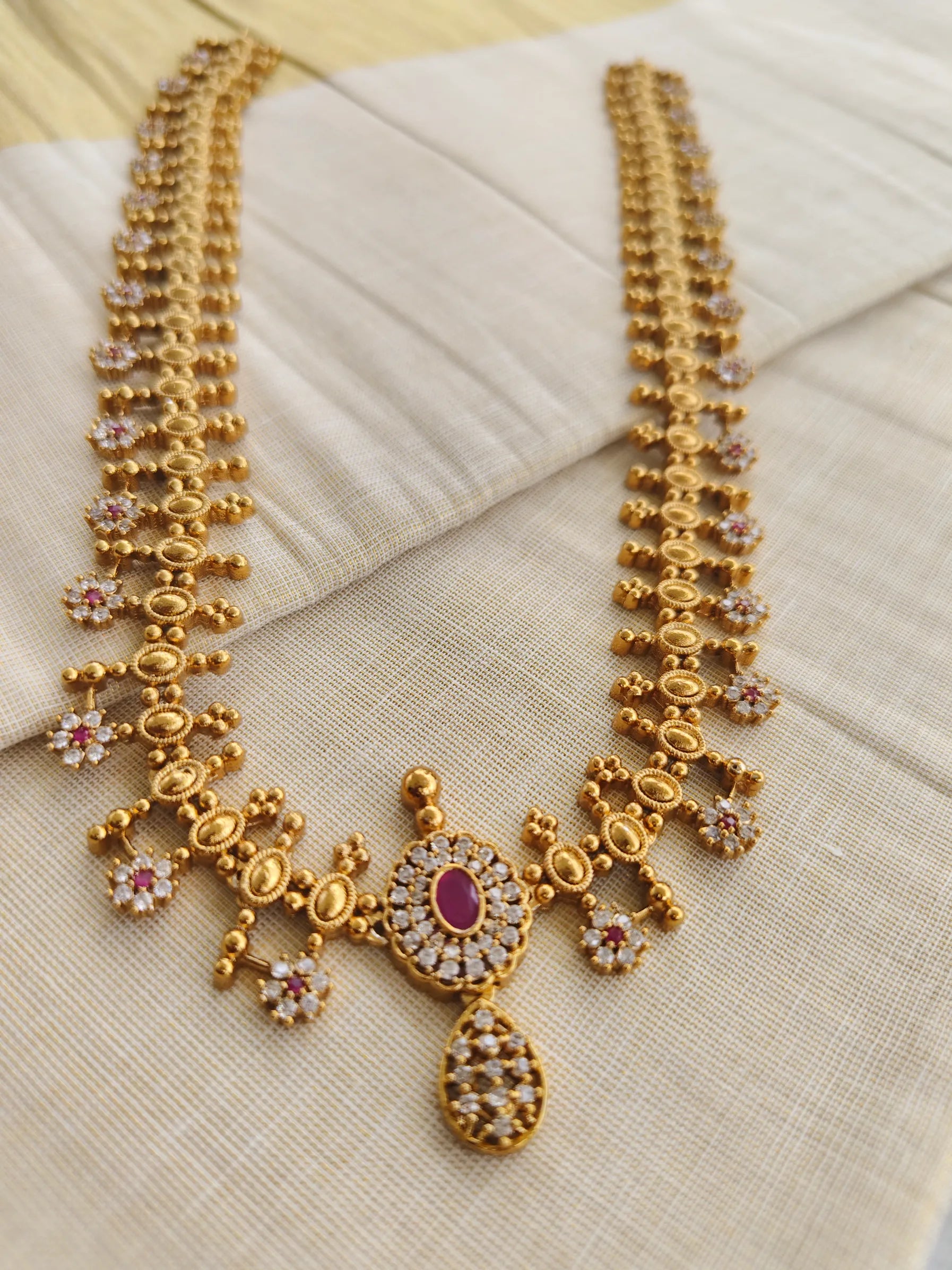 Gold necklace with intricate design and ruby red gemstone on a beige fabric background