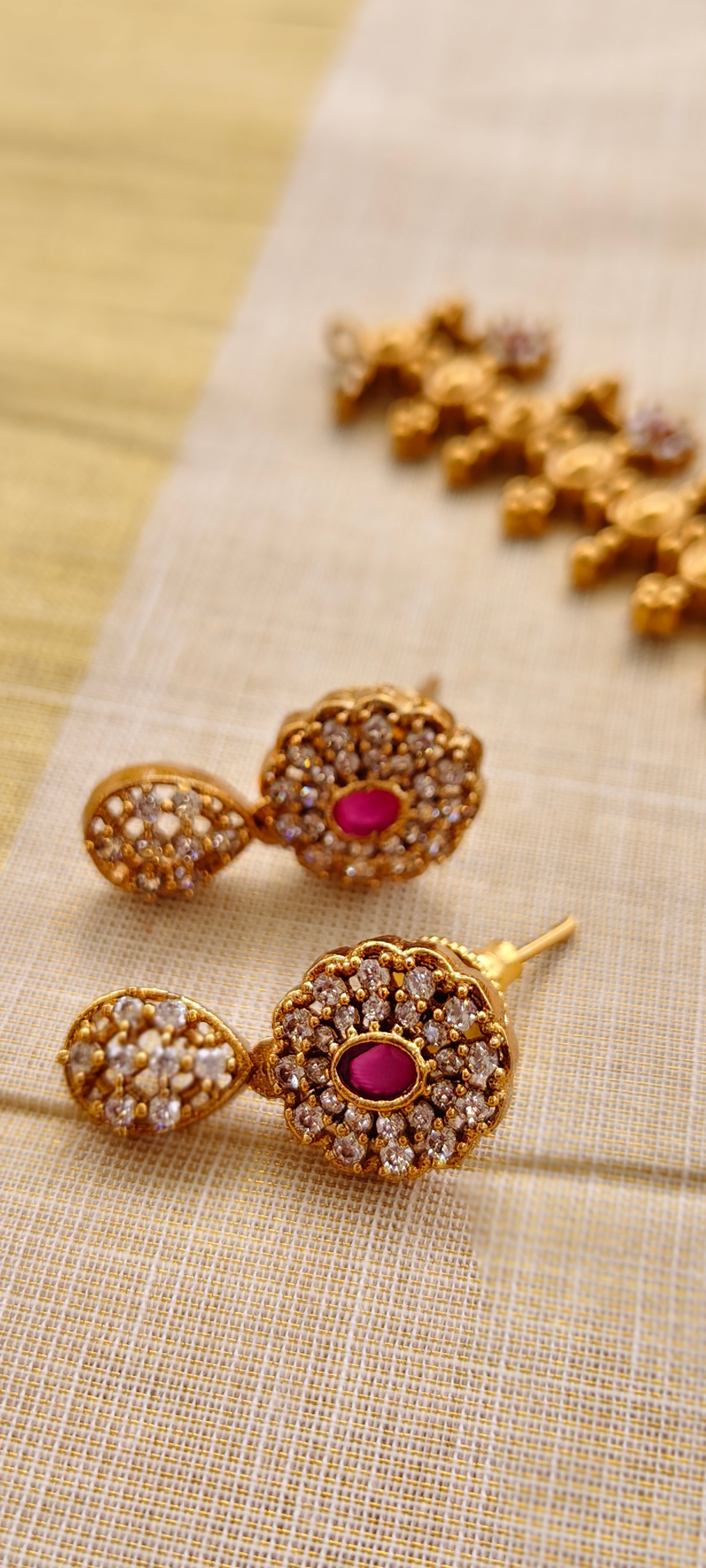 Gold earrings with ruby red gemstones on a beige fabric background