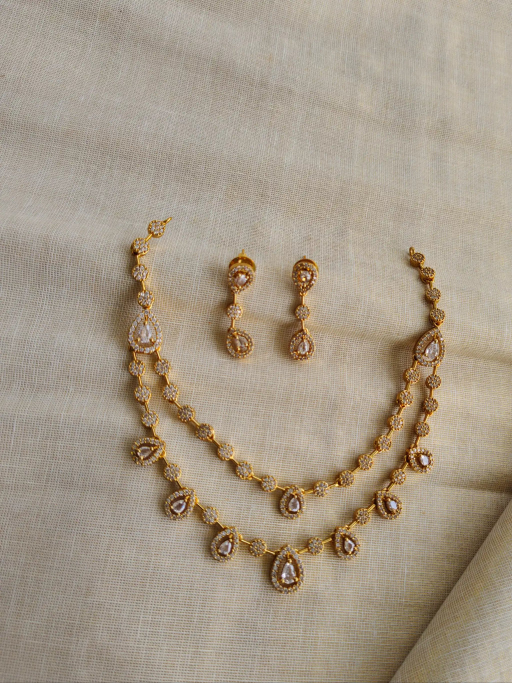 Gold necklace and earrings set on a beige fabric background
