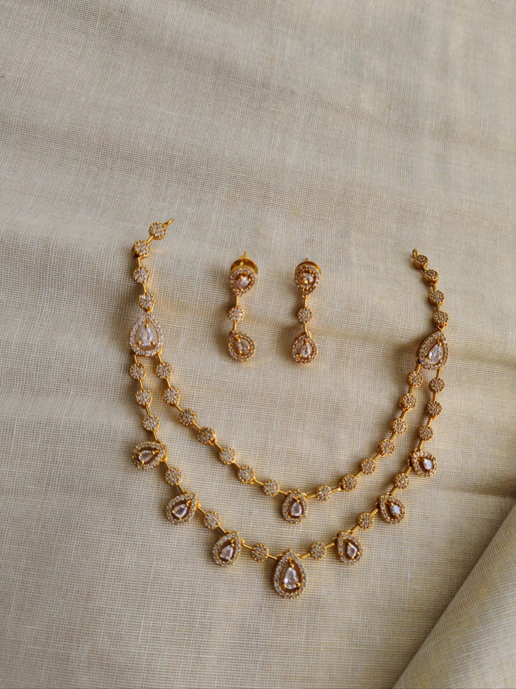 Gold necklace and earrings set on a beige fabric background