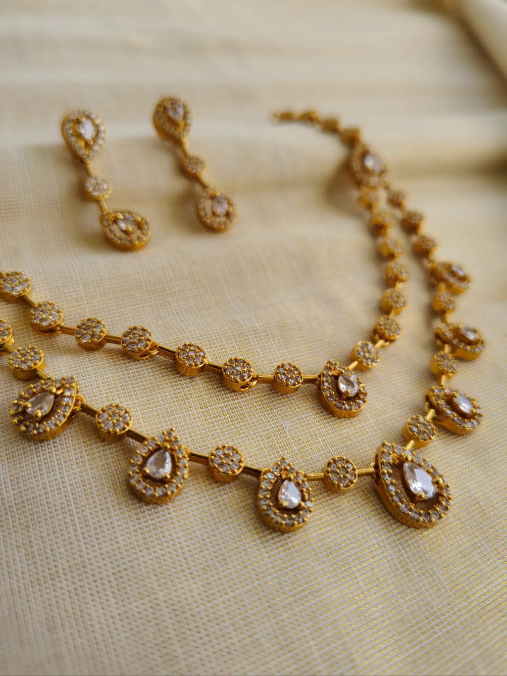 Gold necklace and earrings on a beige fabric background