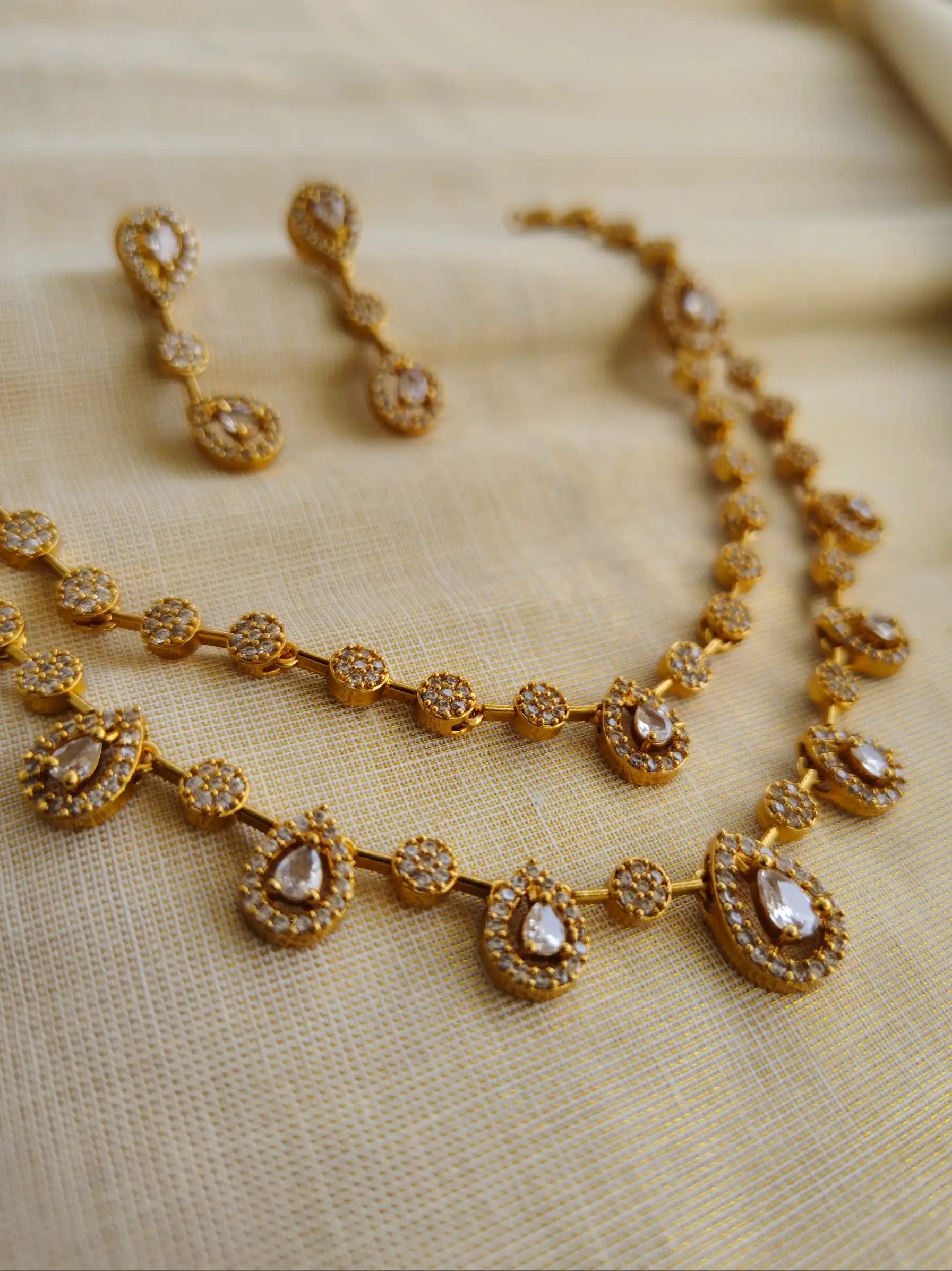 Gold necklace and earrings on a beige fabric background