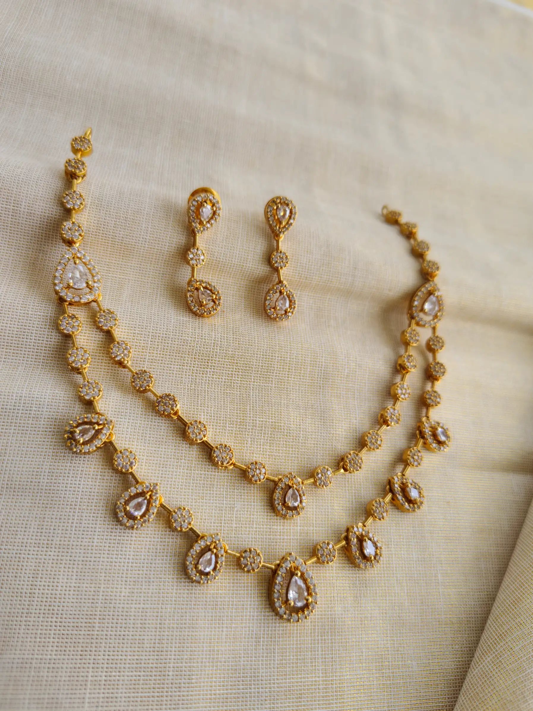 Gold necklace and earrings set on a beige fabric background