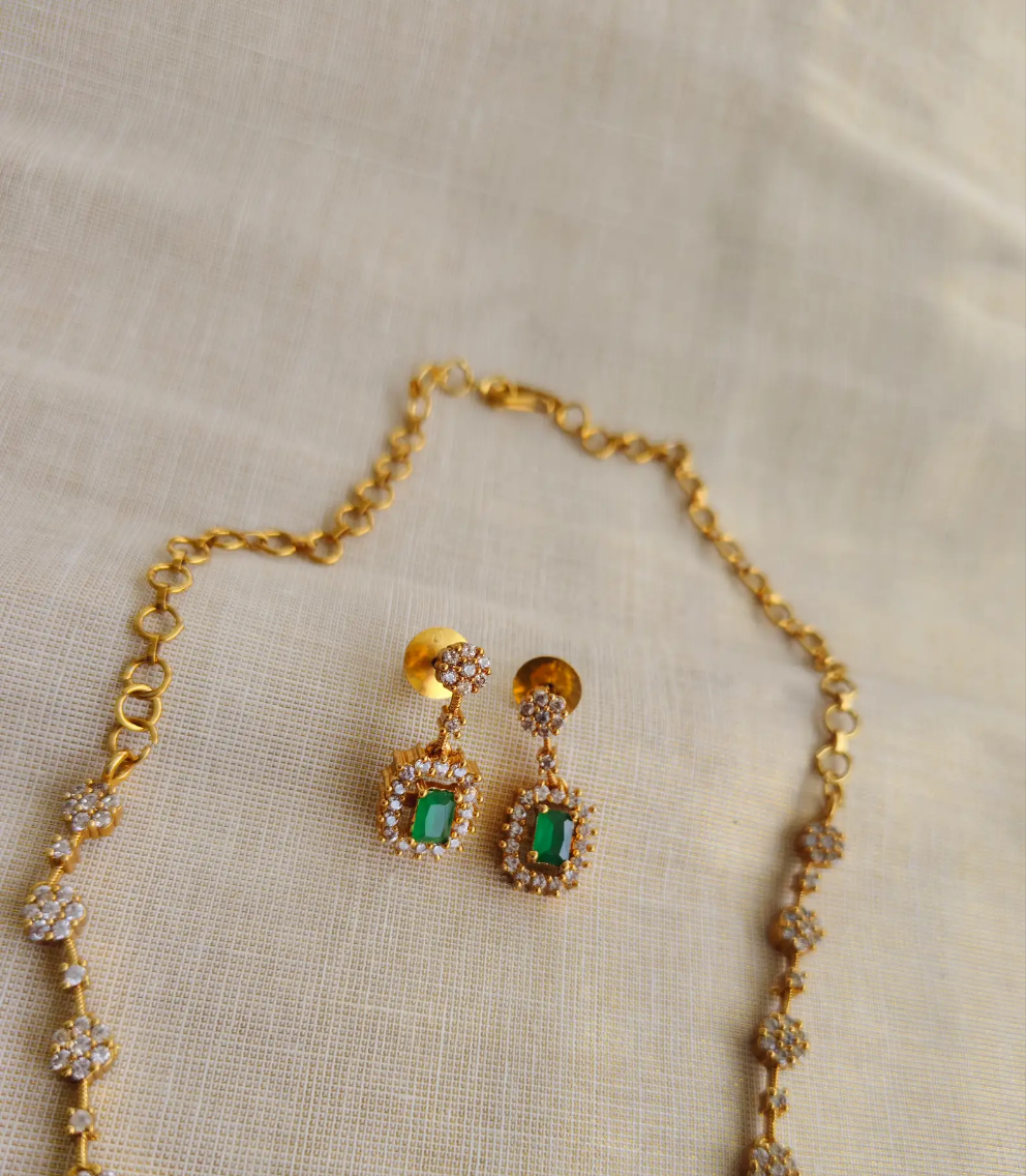 Gold necklace and earrings with green gemstones on a beige fabric background
