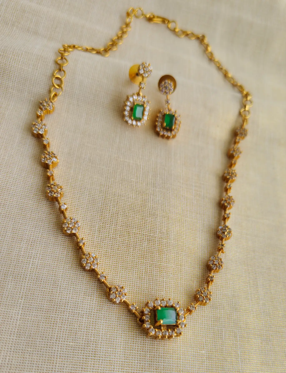 Gold necklace with green gemstones and matching earrings on a beige fabric background