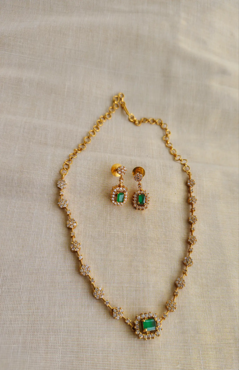 Gold necklace with green gemstones and matching earrings on a beige fabric background