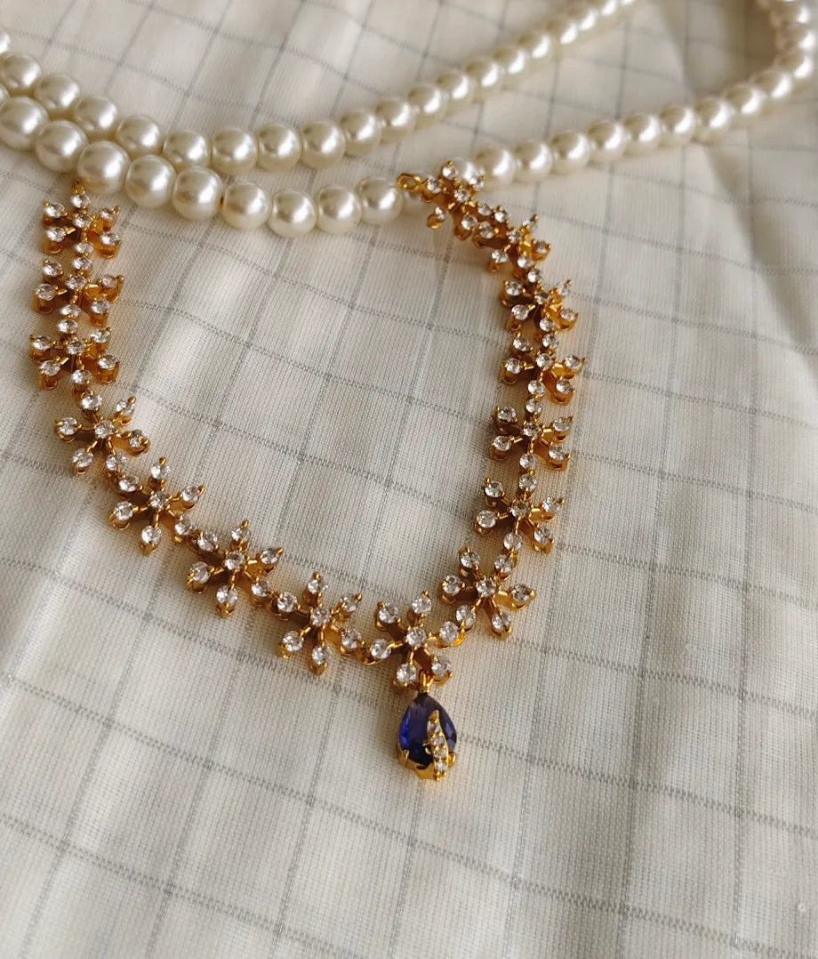Necklace with gold and blue pendant on a checkered fabric background