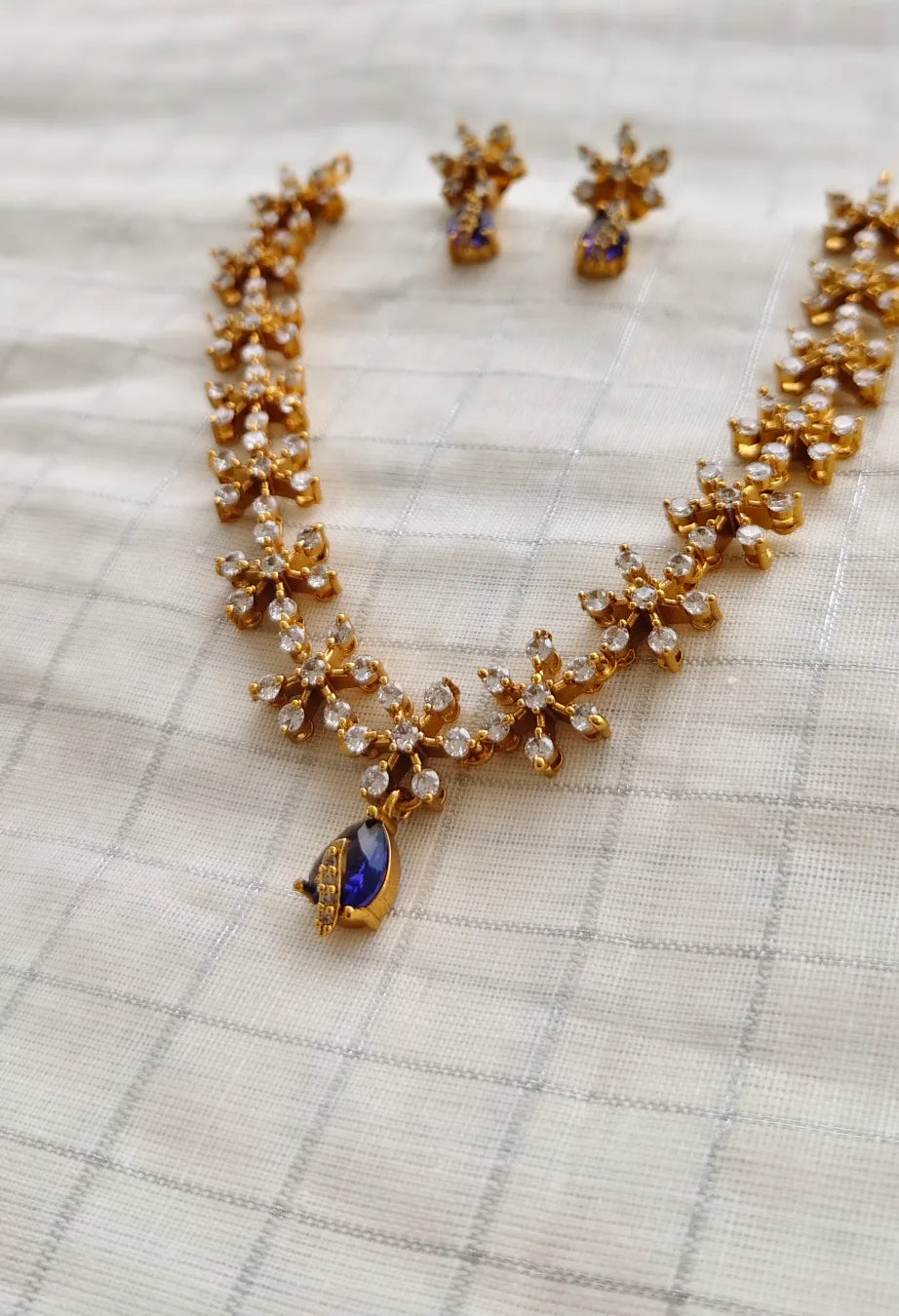 Gold necklace with a blue gemstone and matching earrings on a checkered fabric background