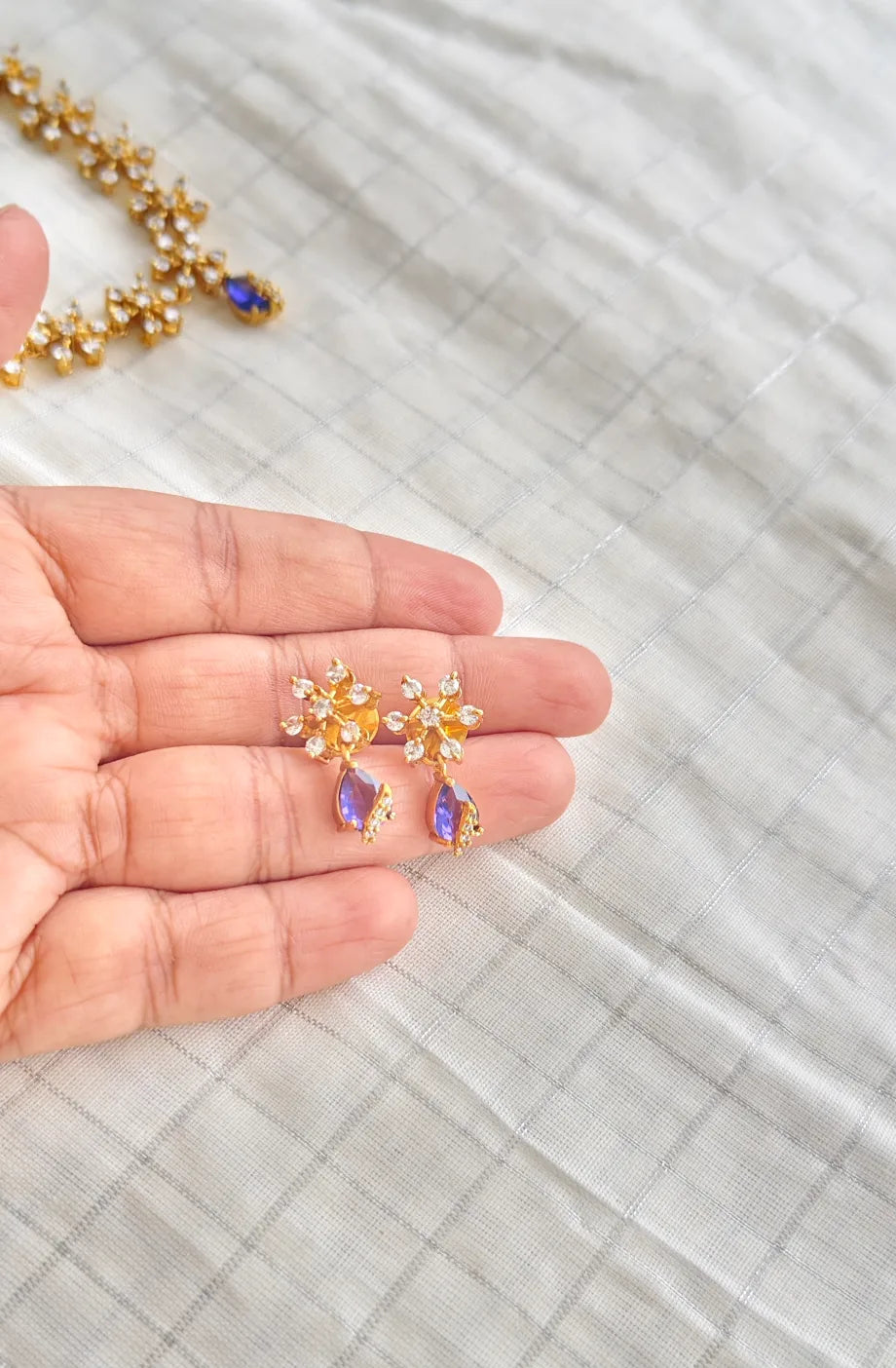 Gold earrings with gemstones held in a hand on a light fabric background