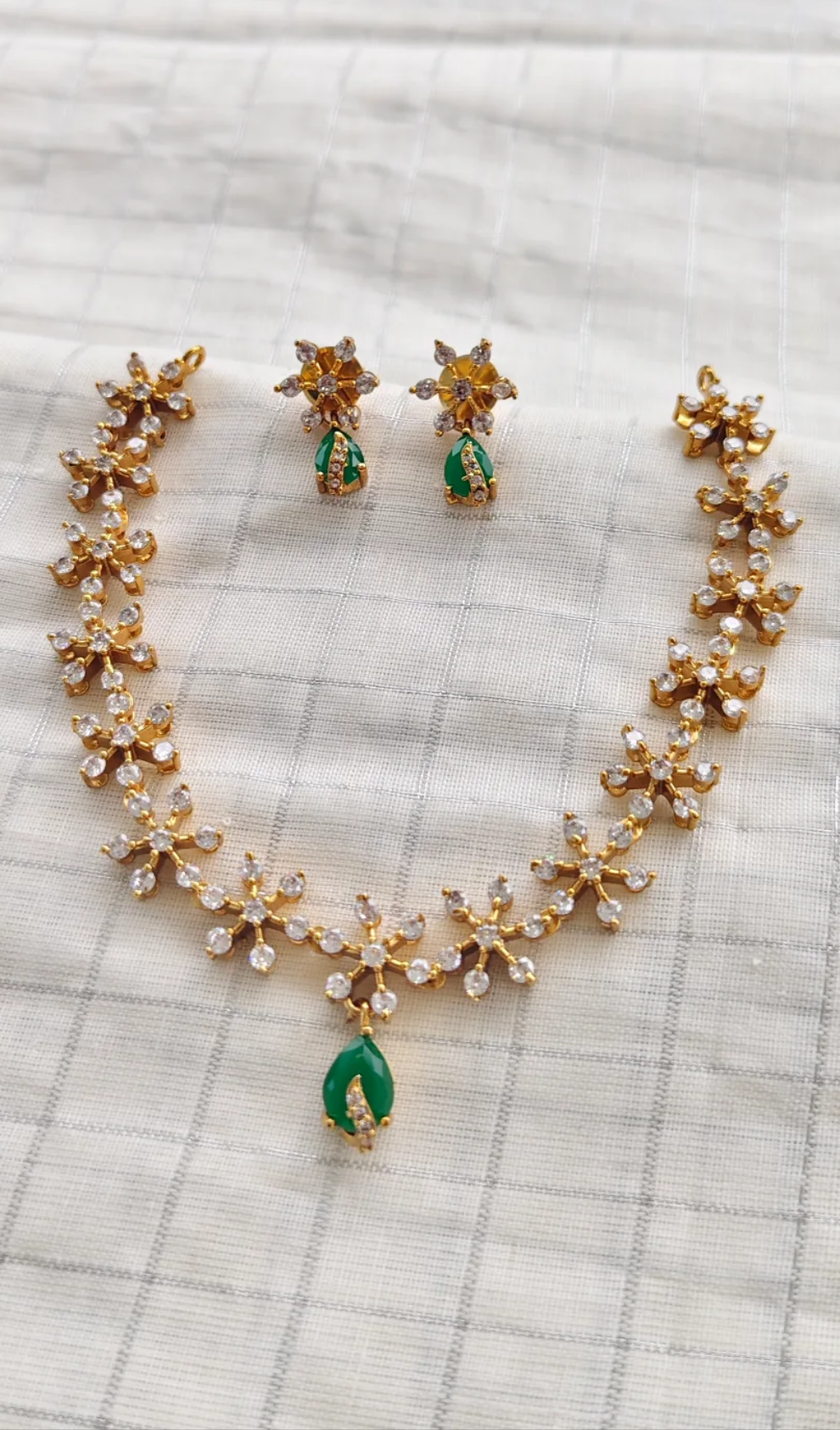 Gold necklace with green stones and matching earrings on a textured surface