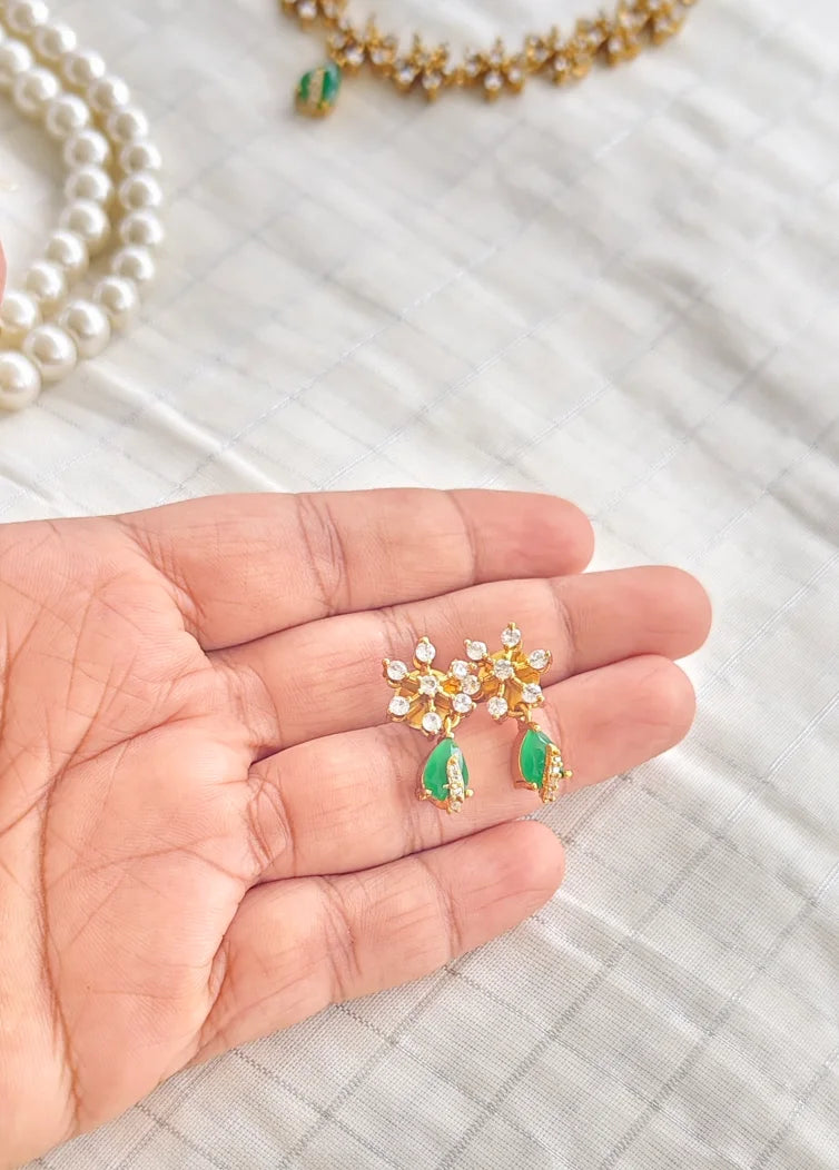 Hand holding a pair of earrings with green gemstones and gold accents on a textured surface.