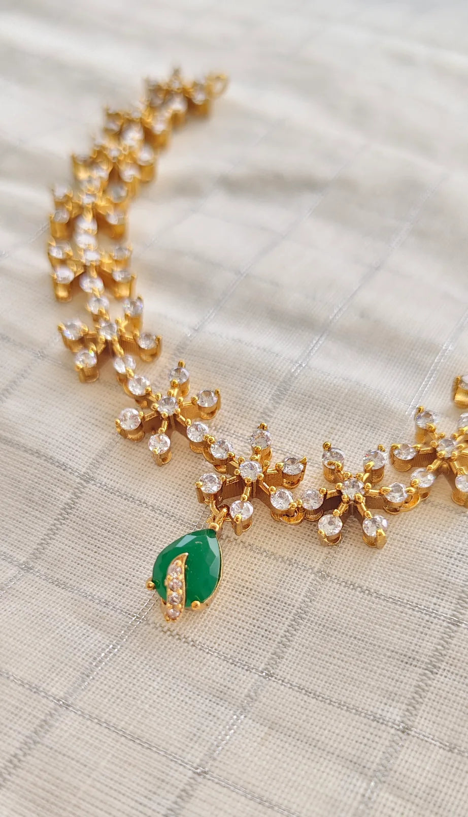 Gold necklace with green gemstone on a textured beige background