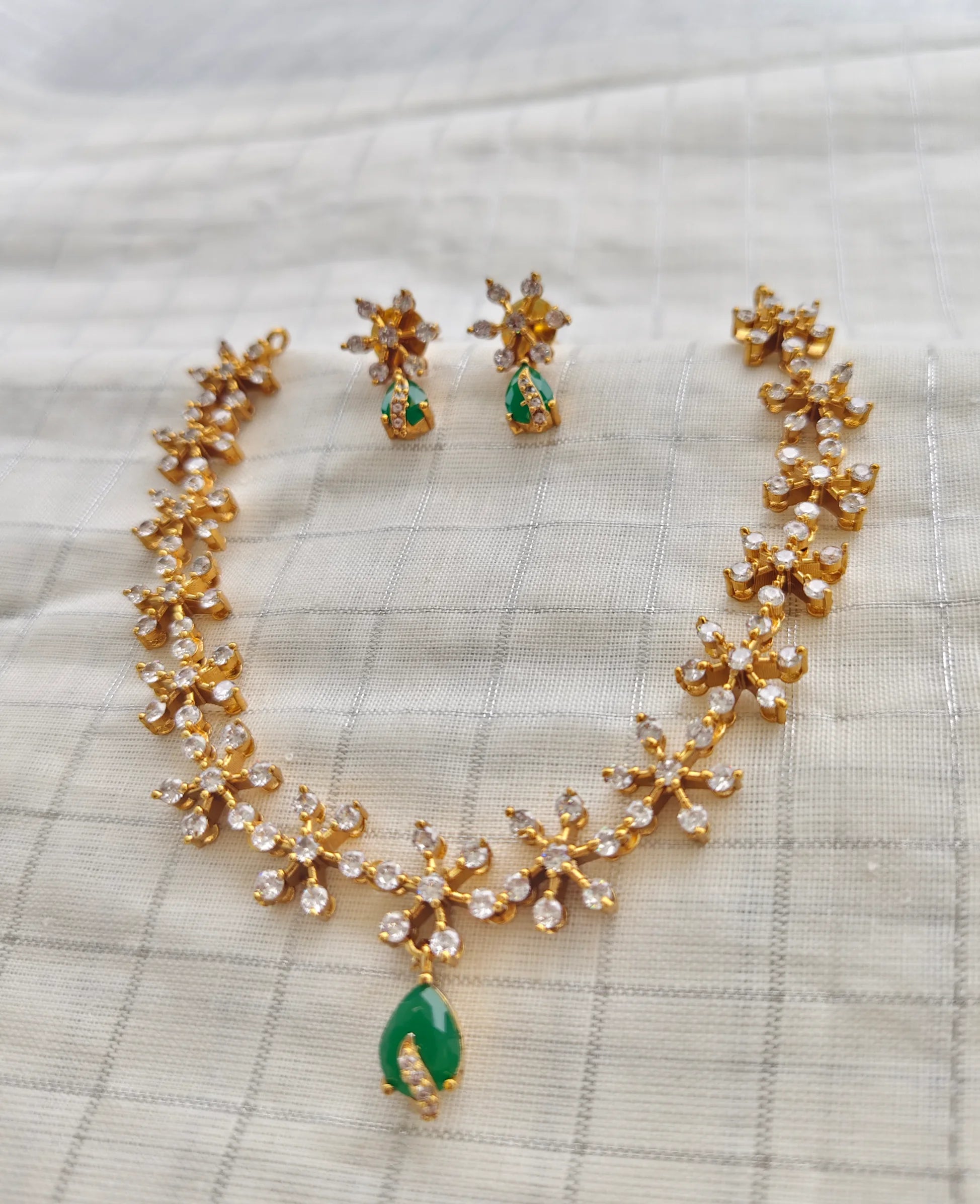 Gold necklace with green stones and matching earrings on a textured fabric background