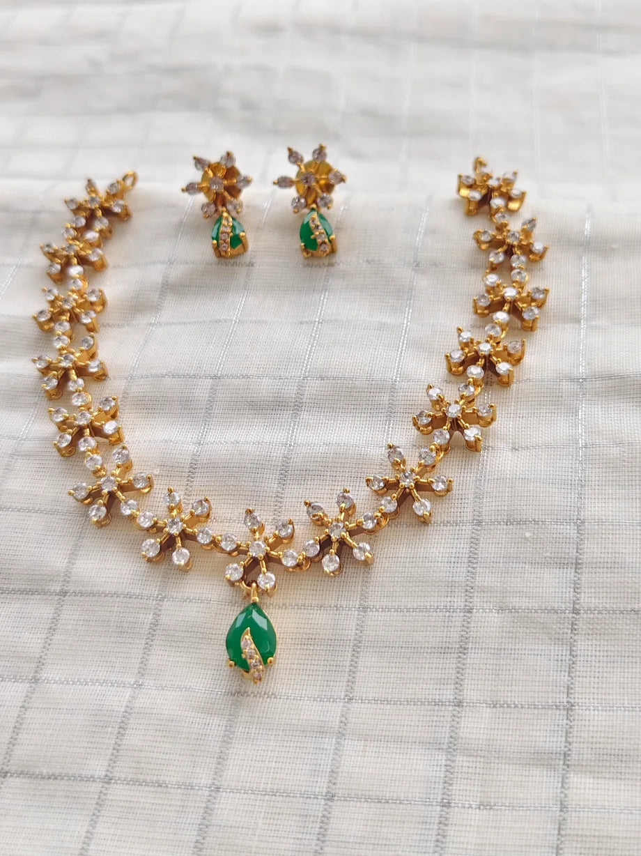 Gold necklace with green teardrop pendants and matching earrings on a checkered fabric background