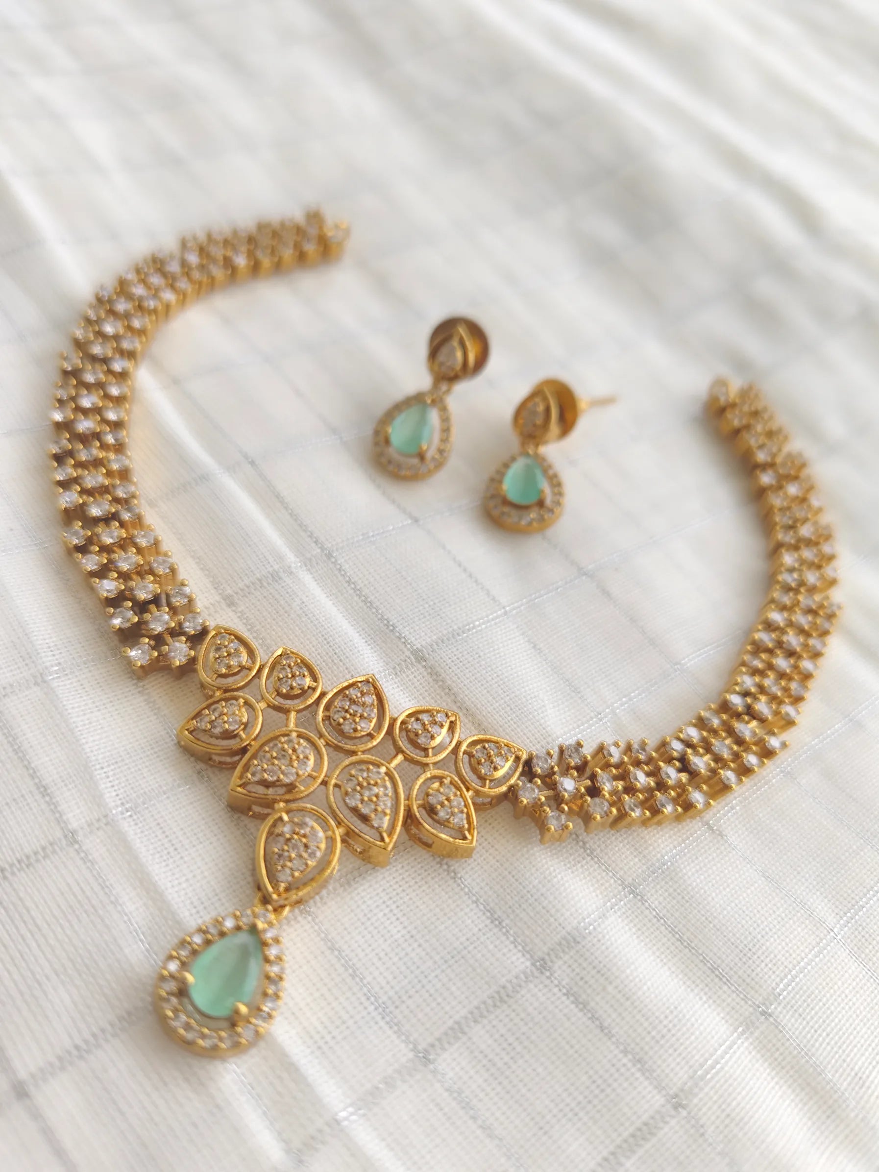 Gold necklace with green stones and matching earrings on a white fabric background