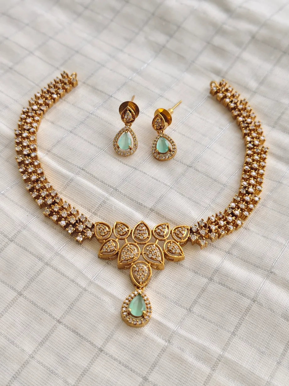 Gold necklace and earrings with green gemstones on a textured surface