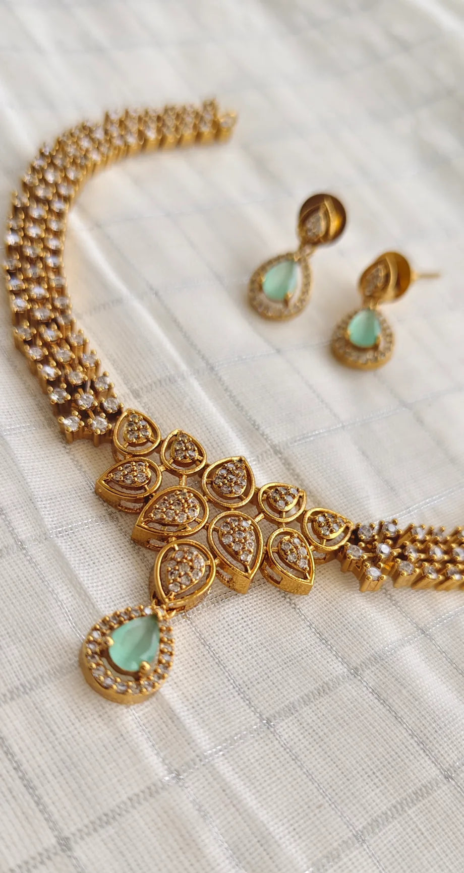 Gold necklace and earrings with green gemstones on a textured white surface