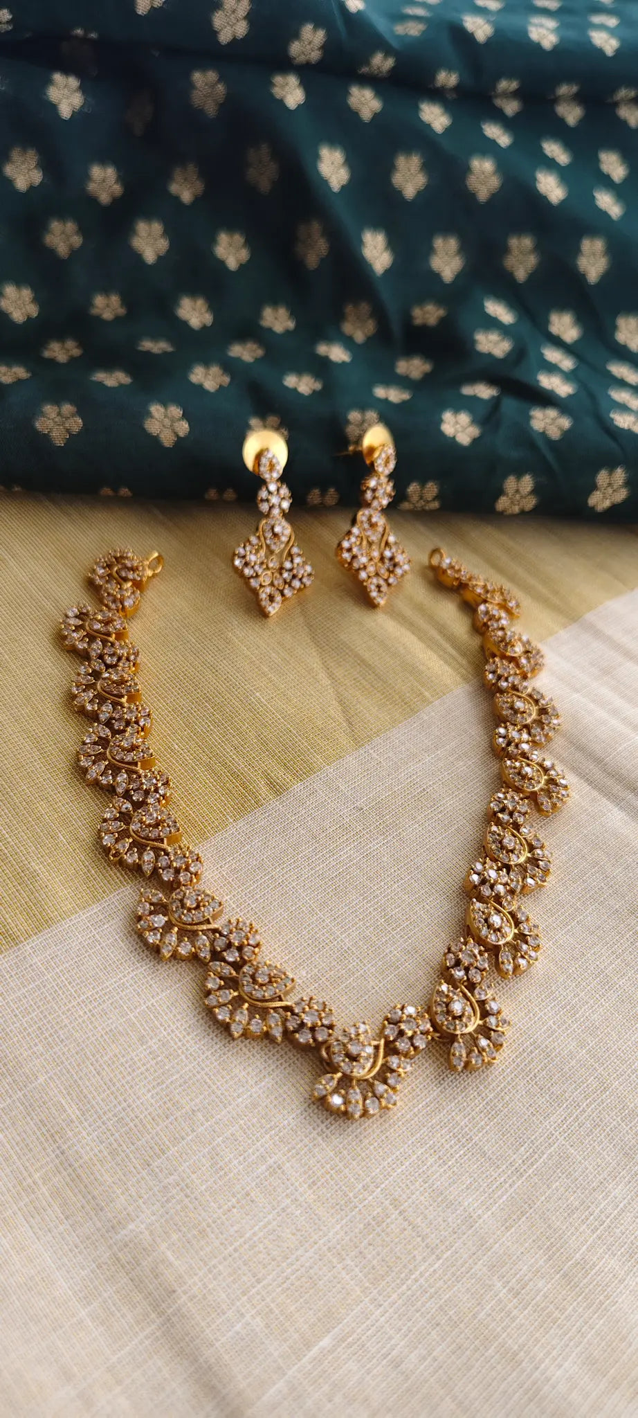 Gold necklace and earrings on a textured surface with a patterned fabric background