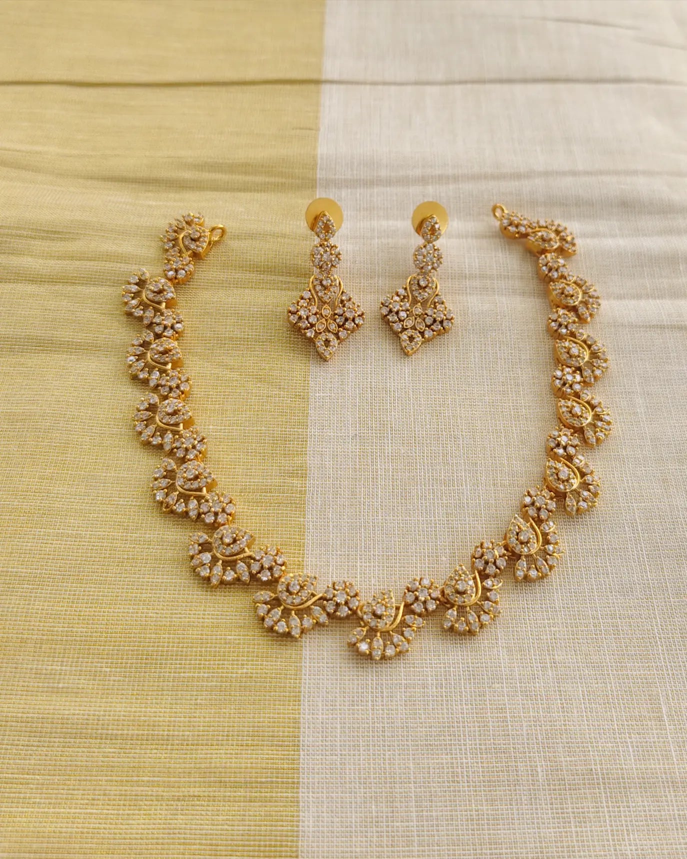 Gold necklace and earrings set on a yellow and white fabric background