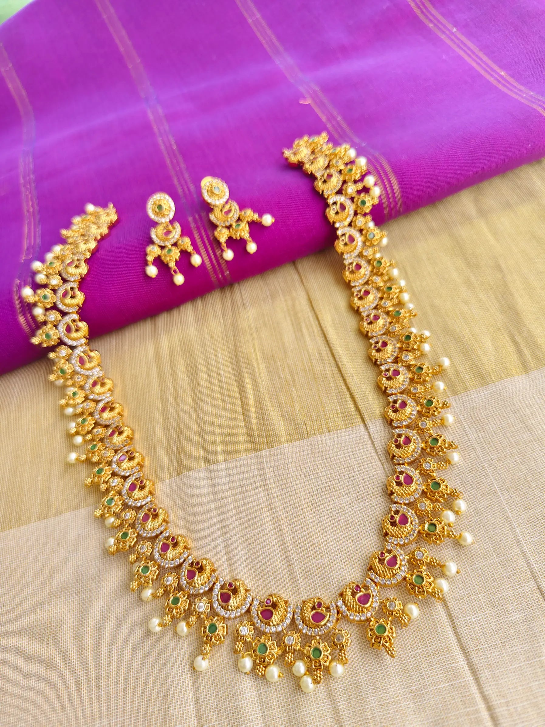 Gold necklace with red and green stones on a purple fabric background