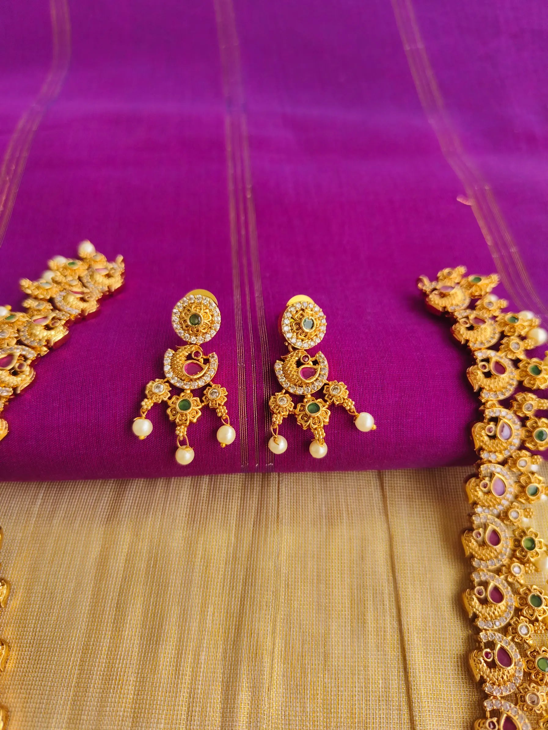 Gold earrings with green and red stones on a purple fabric background