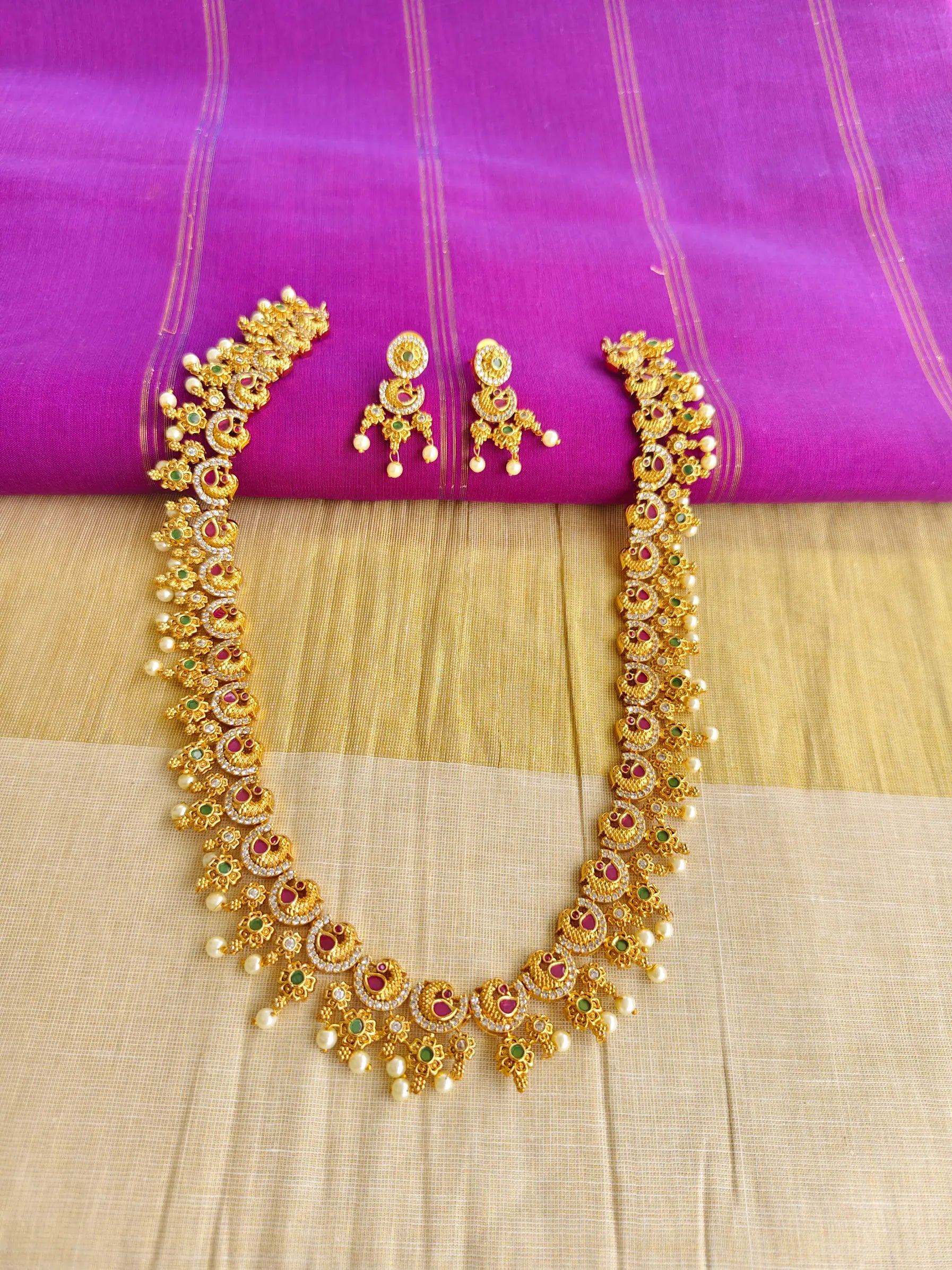 Gold necklace and earrings on a pink and beige fabric background