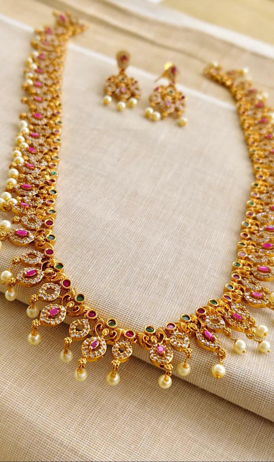 Gold necklace with gemstones and matching earrings on a beige fabric background