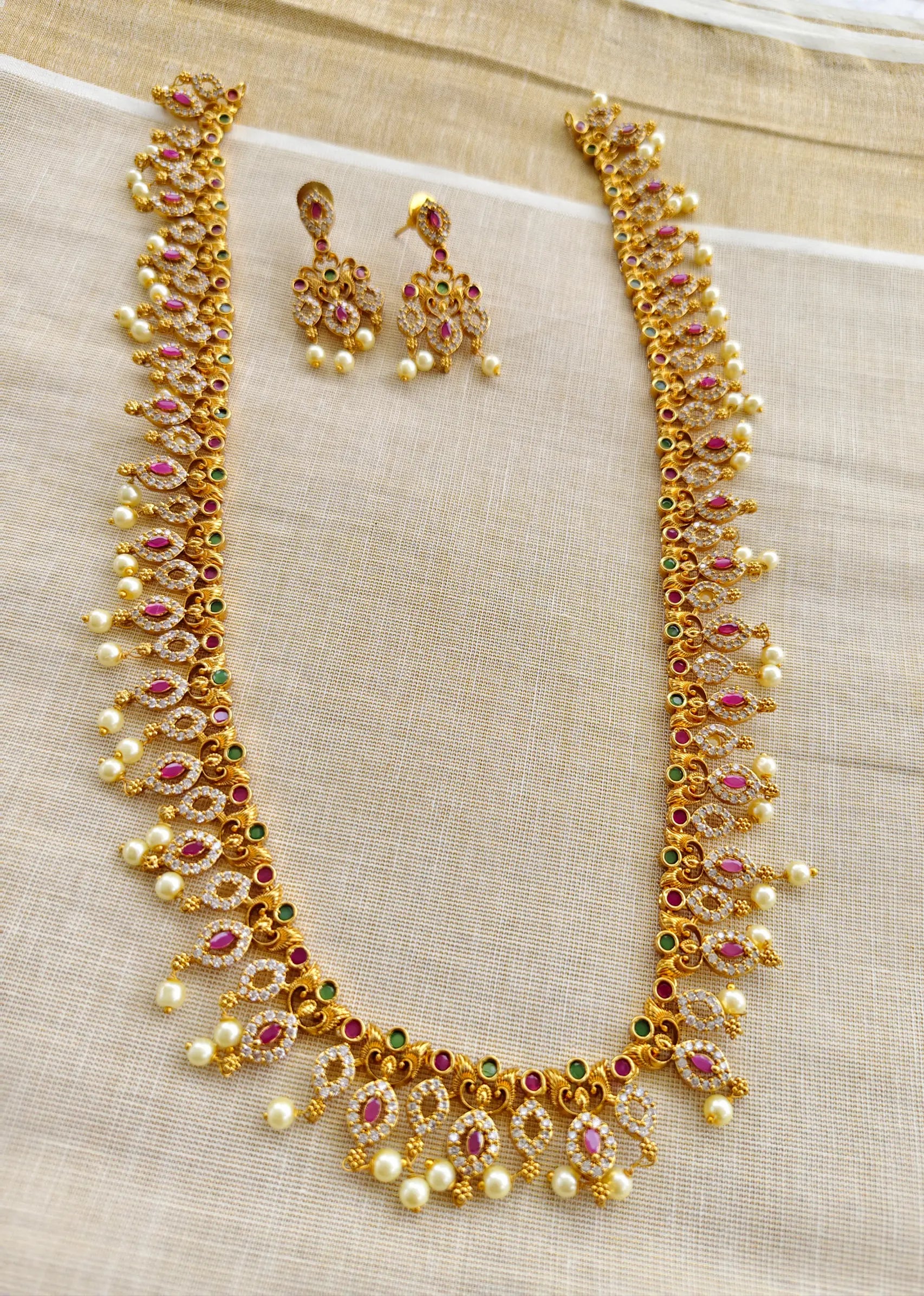 Gold necklace and earrings set on a beige fabric background