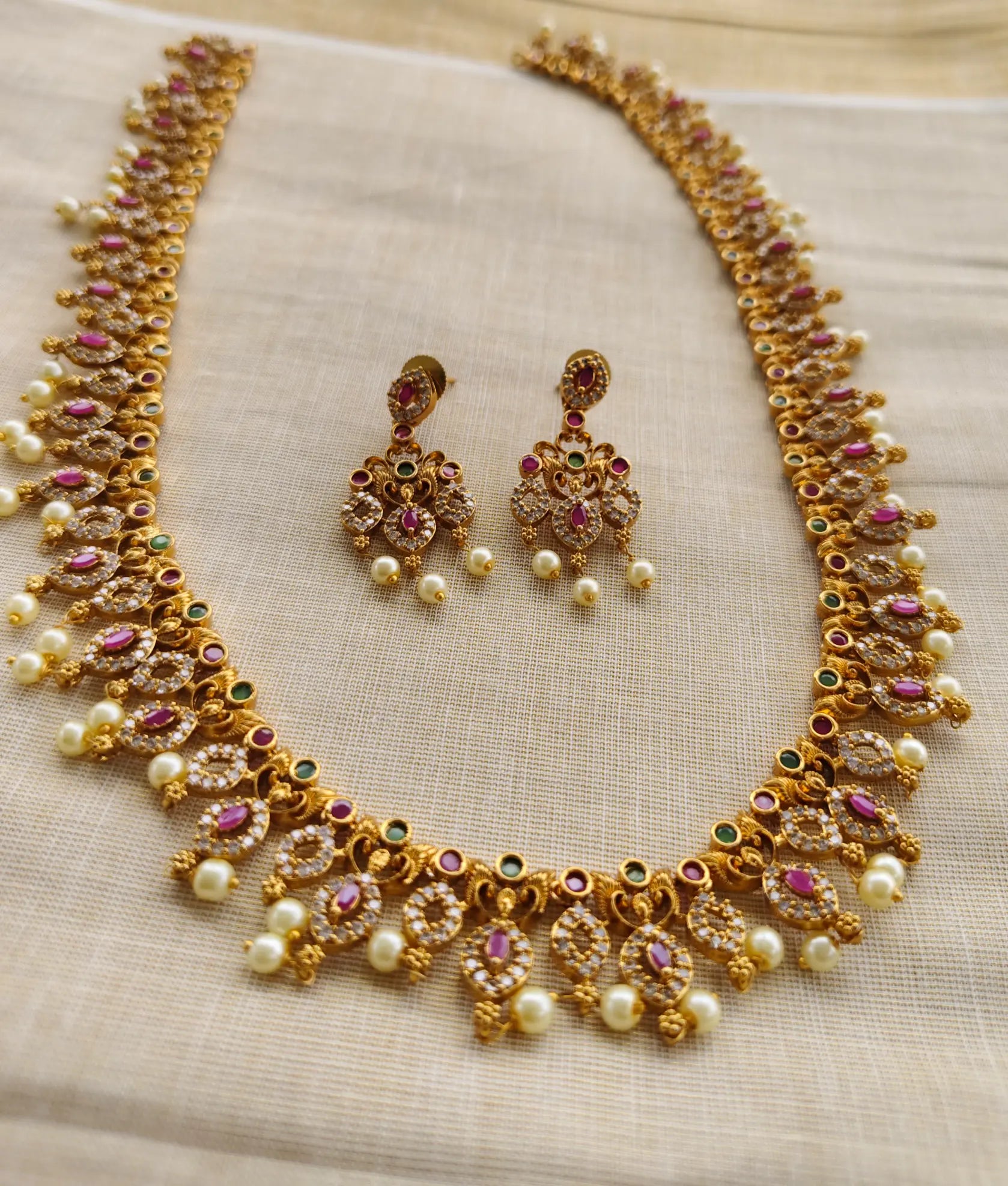 Gold necklace and earrings set on a beige fabric background