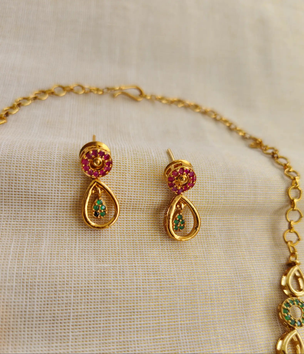 Gold jewelry set with earrings and a necklace on a beige fabric background