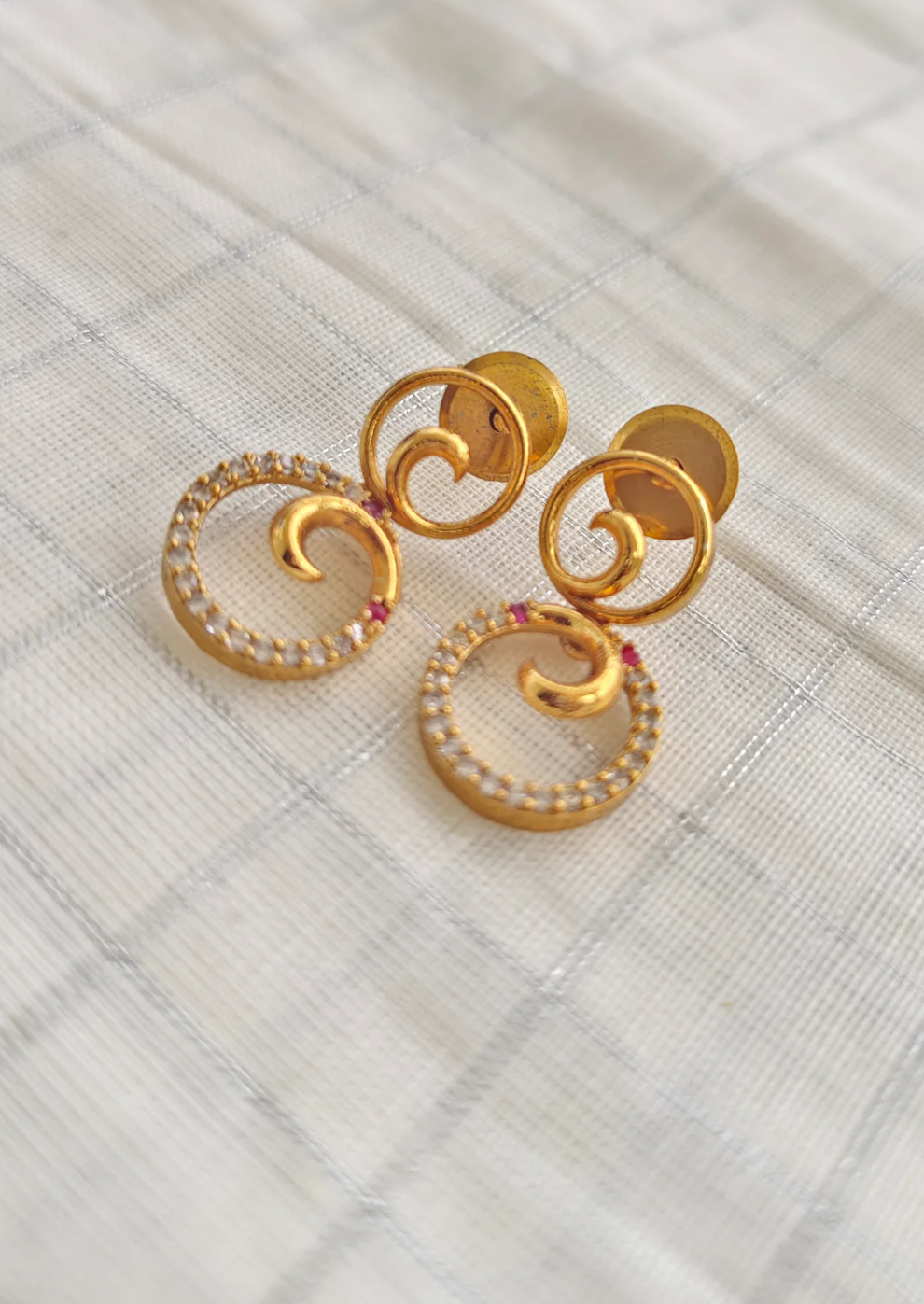 Gold earrings with circular design on a textured white surface