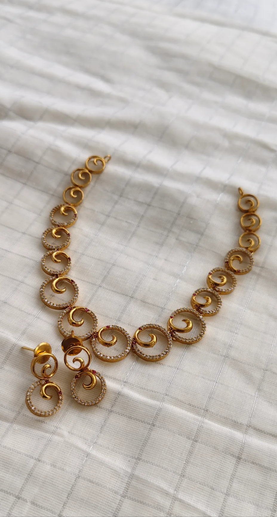 Gold necklace and earrings on a white fabric background