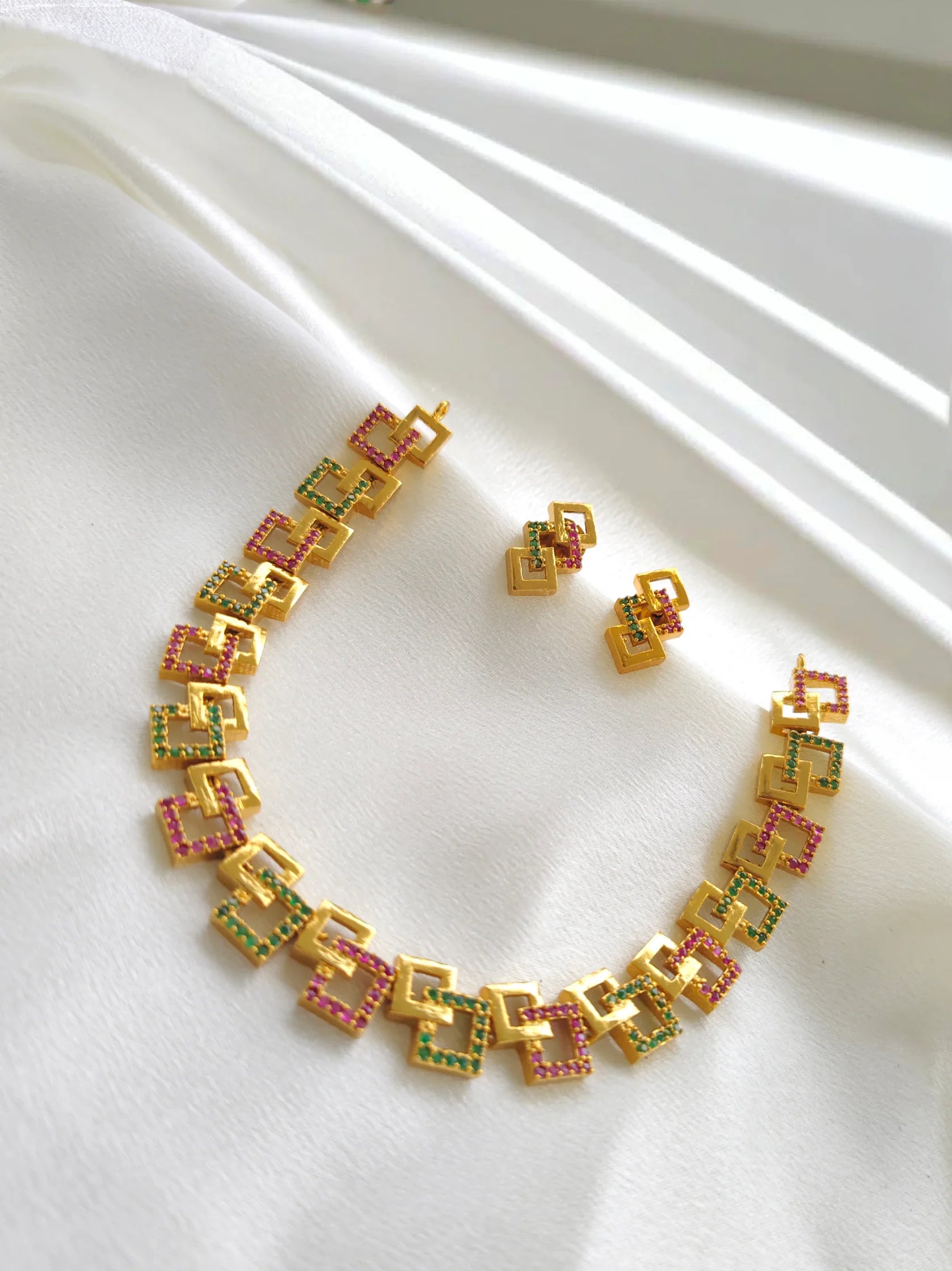 Gold necklace and earrings with colorful gemstones on a white fabric background