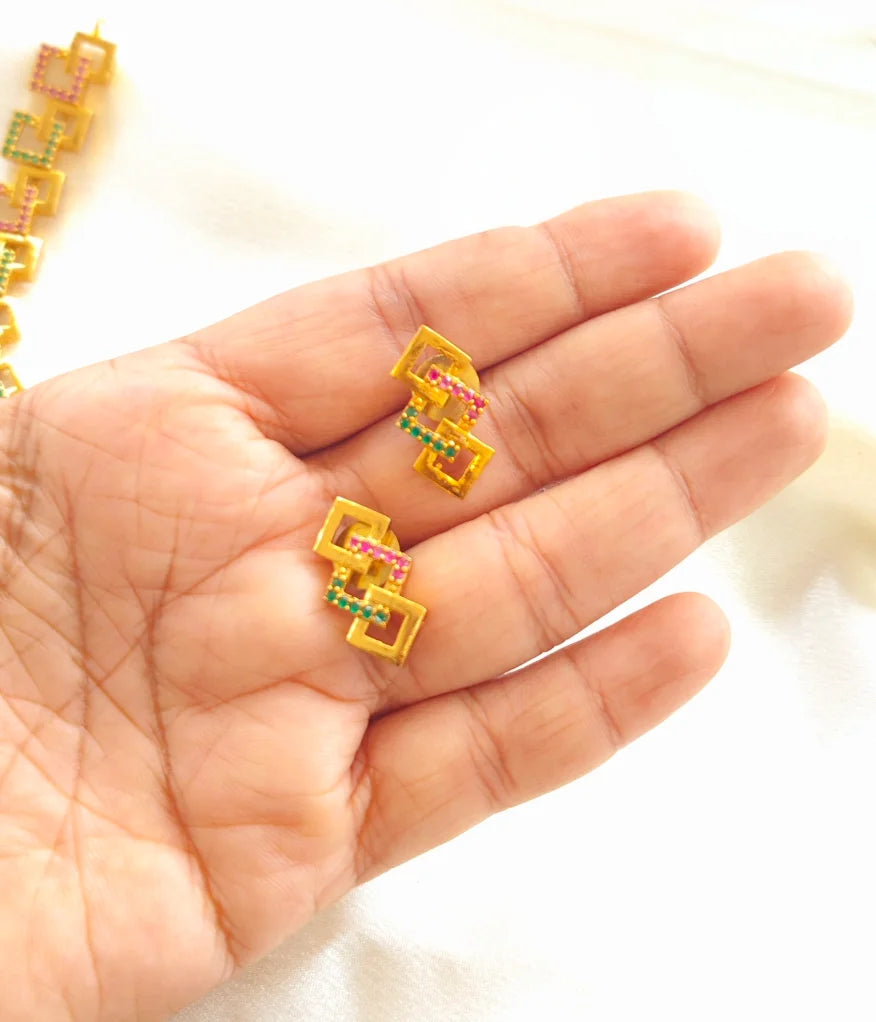 Gold earrings with colourful gem stones held by a hand