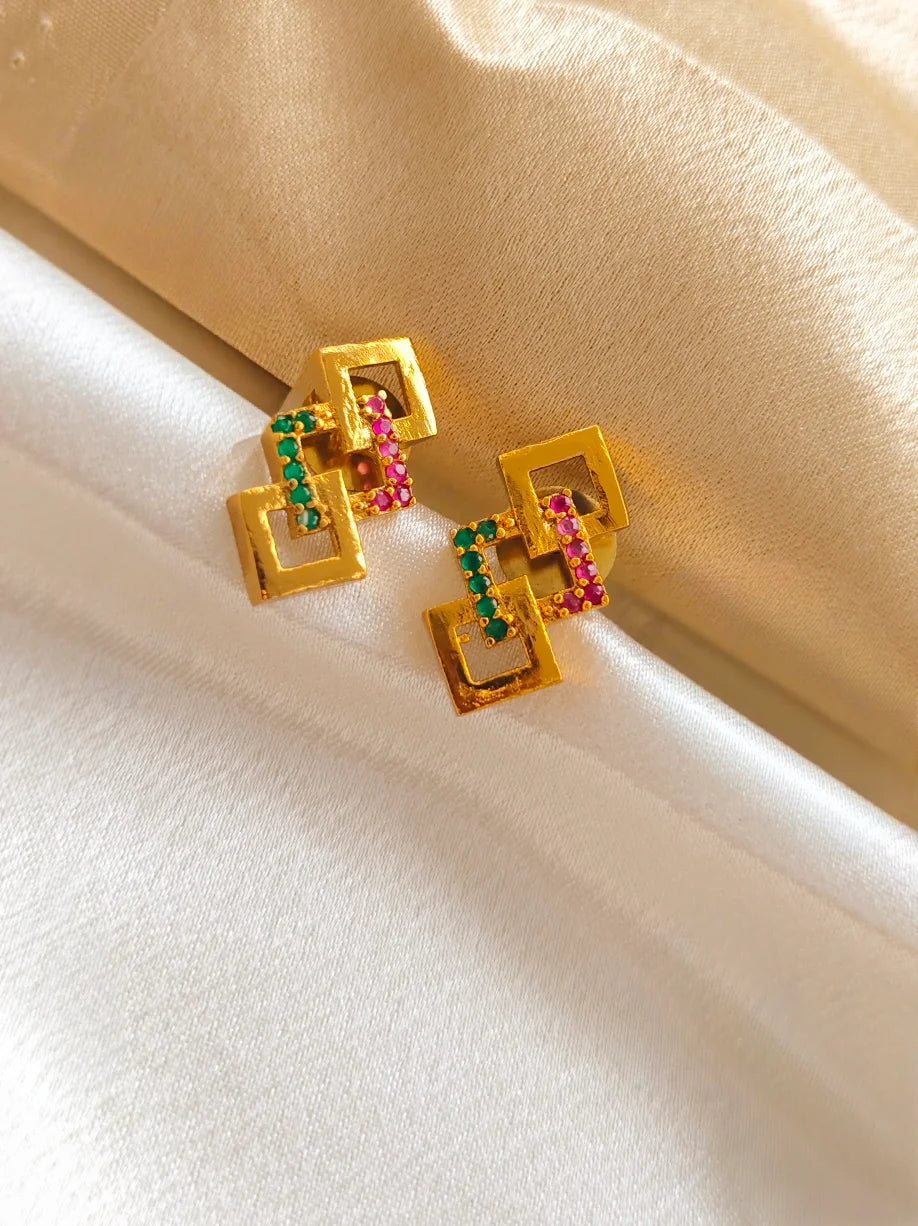 Gold earrings with colorful gemstones on a white and beige fabric background