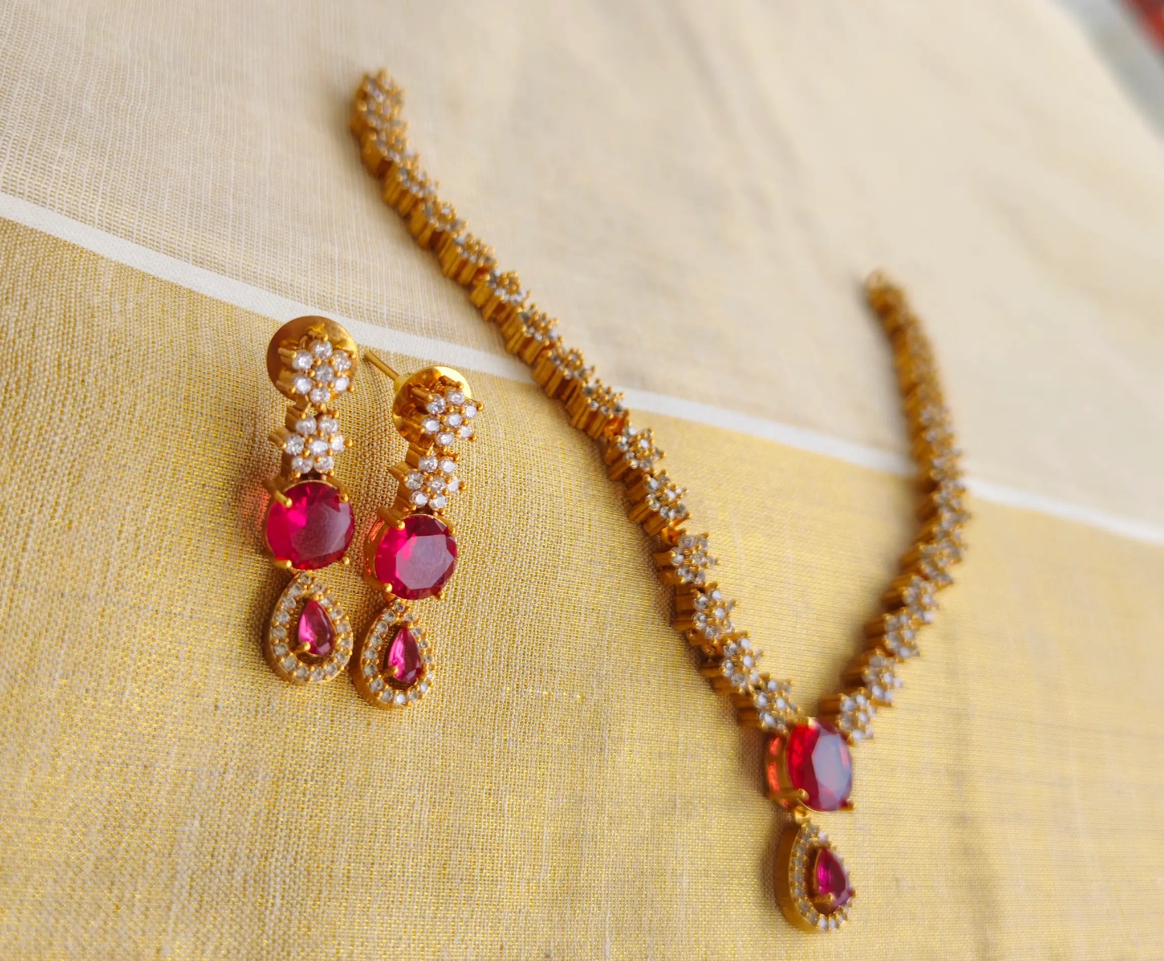 Gold necklace with red gemstones and matching earrings on a beige fabric background