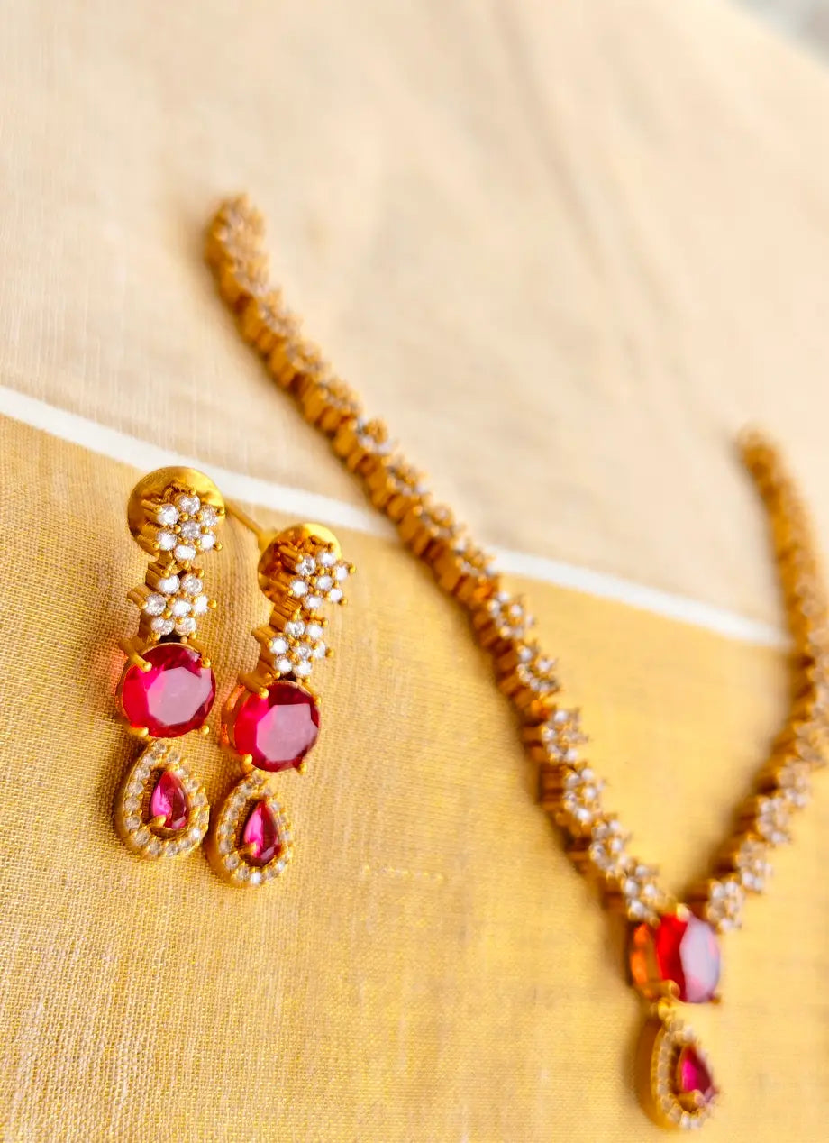 Pair of gold earrings with red stones and a matching necklace on a beige background