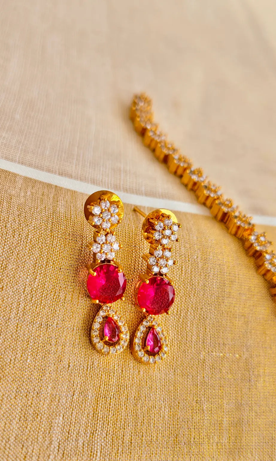 Pair of red teardrop earrings with gold accents on a beige fabric background