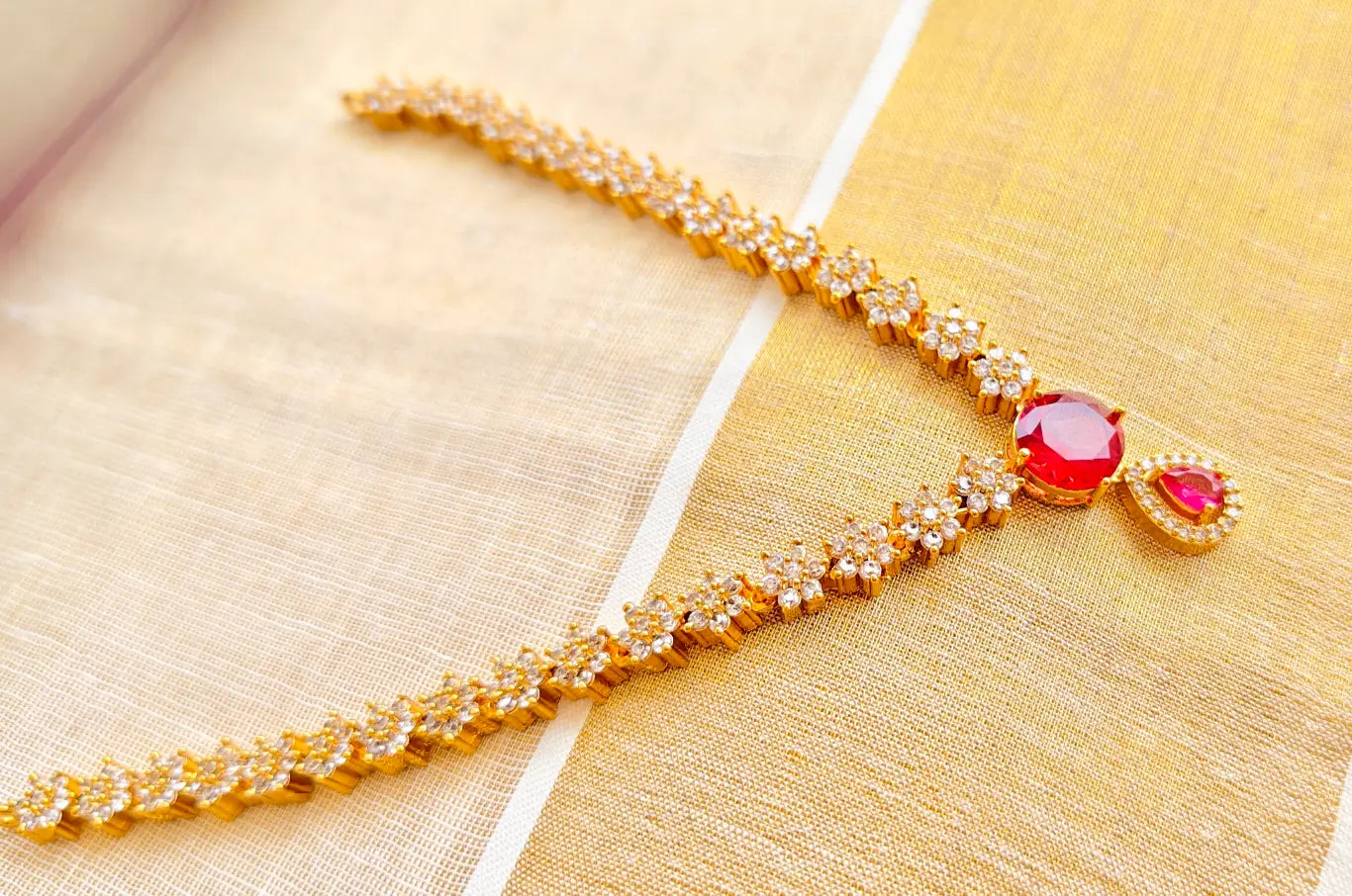 Gold necklace with red gemstones on a gold fabric background