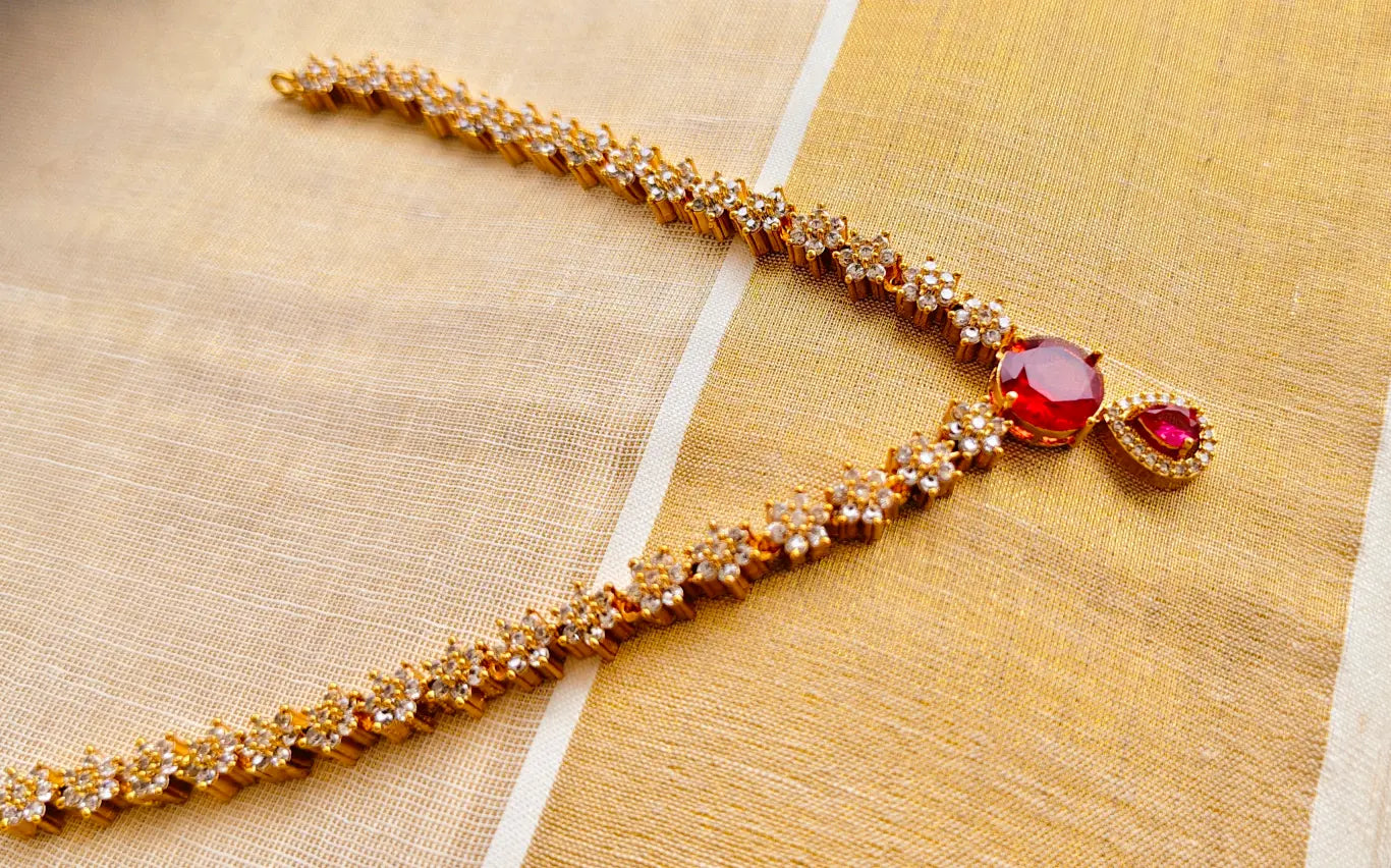 Gold necklace with red gemstones on a textured beige background