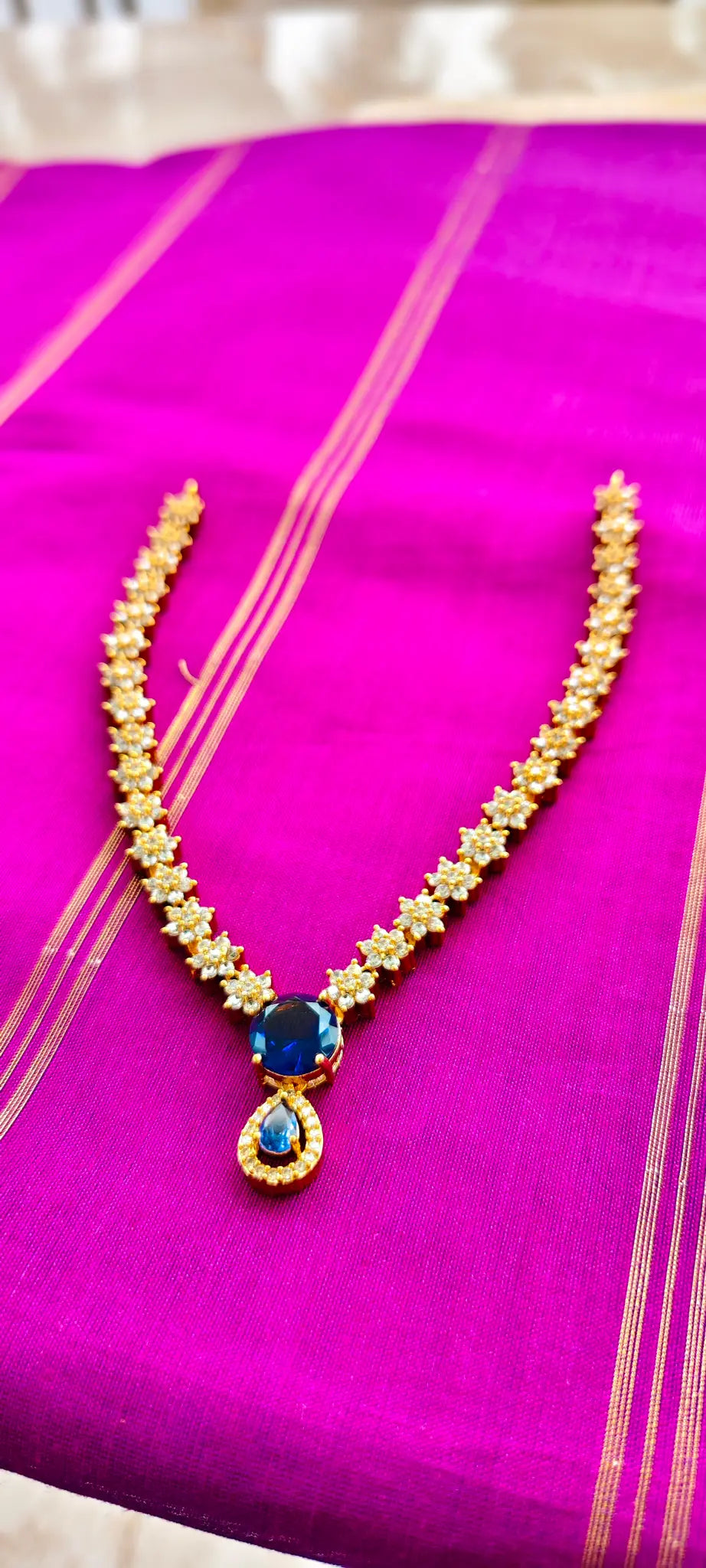 Gold necklace with a blue pendant on a pink fabric background