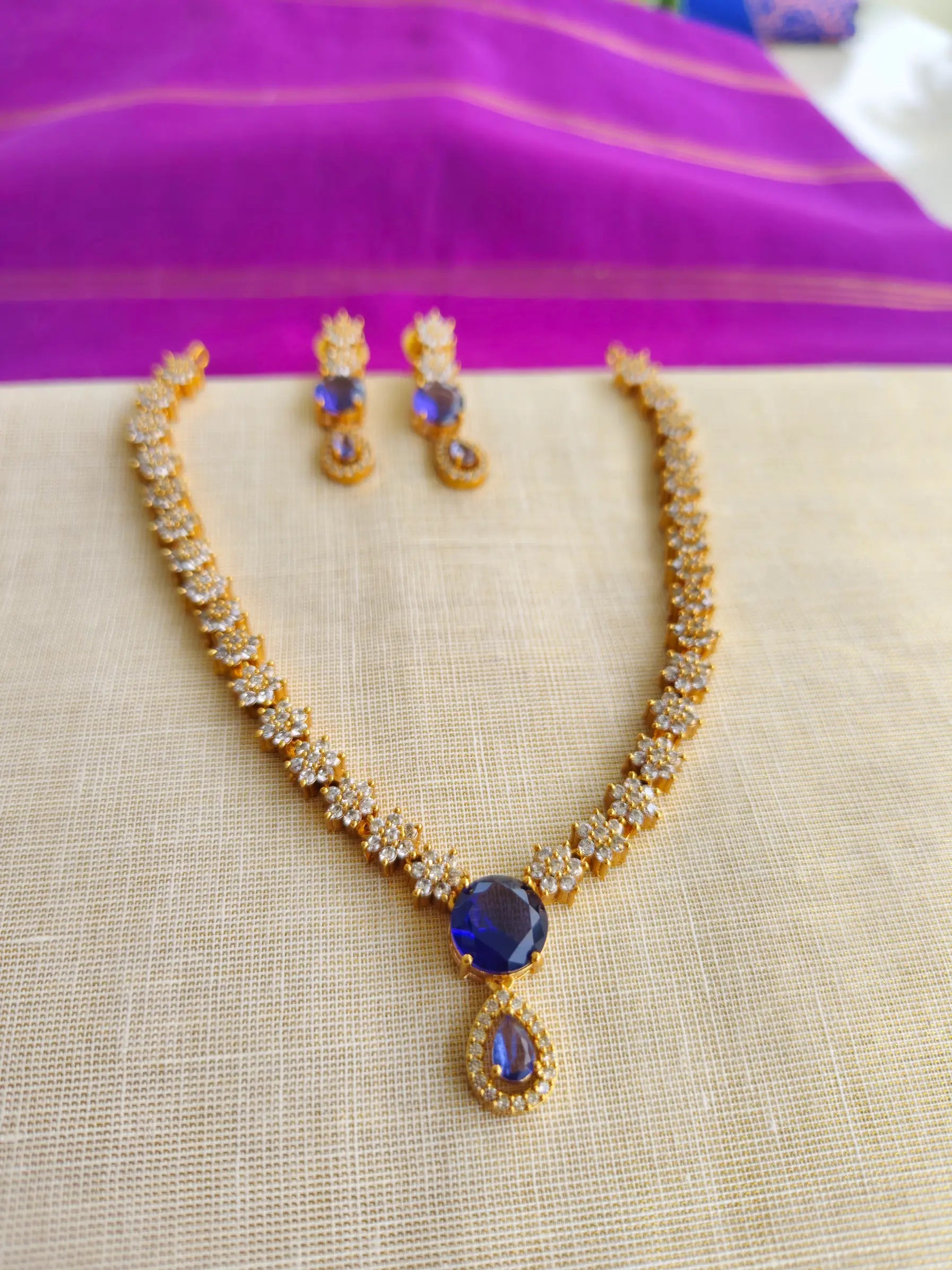 Gold necklace with blue stone and matching earrings on a beige surface.