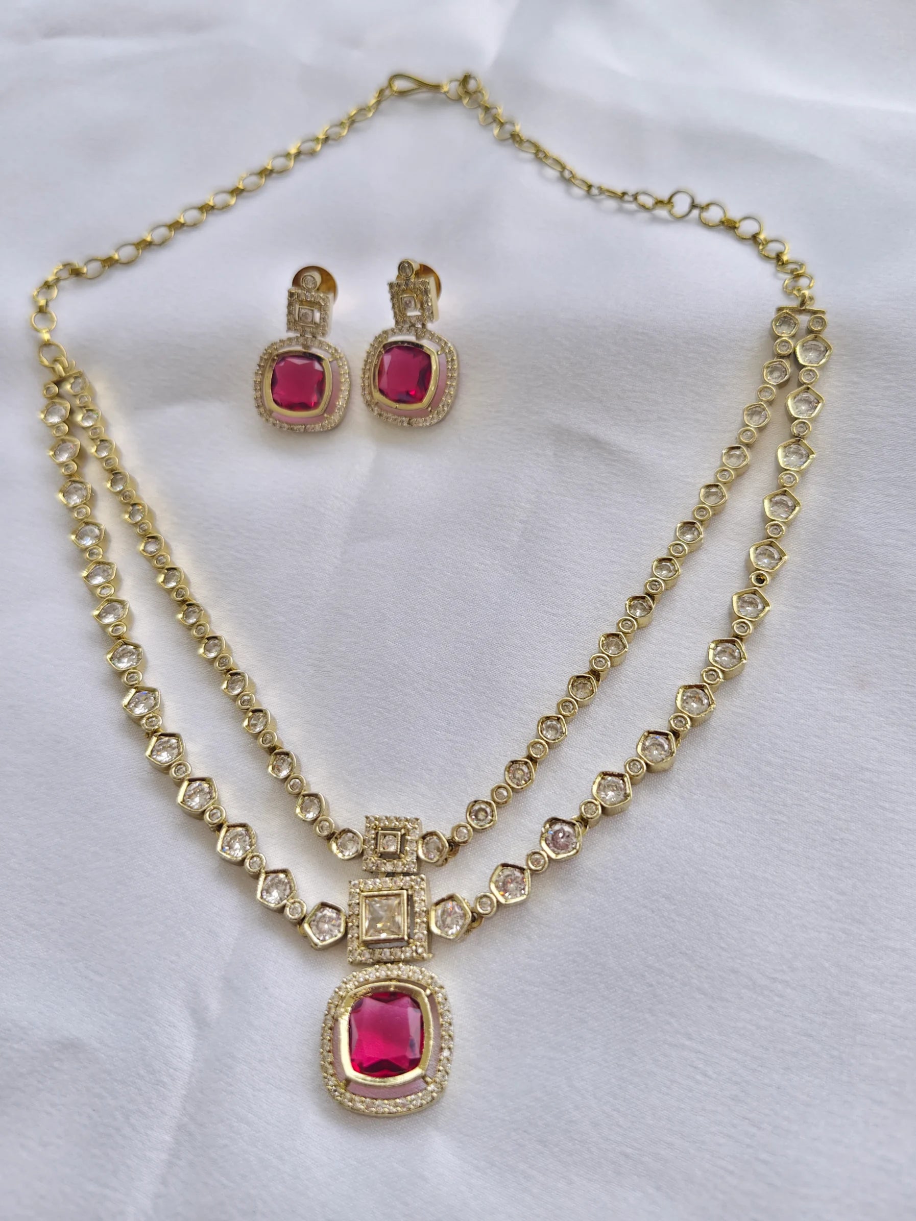 Gold necklace with a red gemstone and matching earrings on a white background