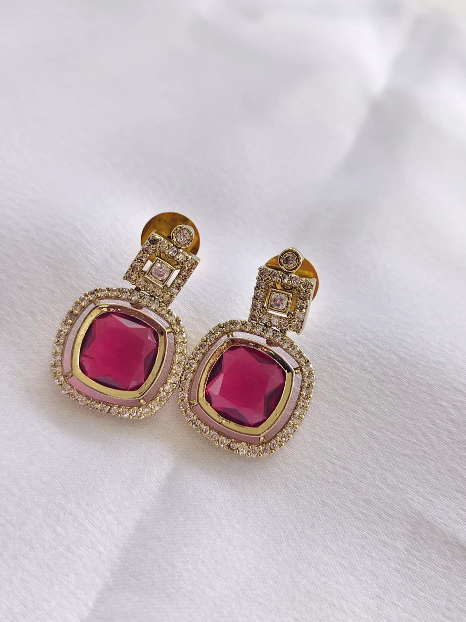 Gold earrings with pink gemstones on a white fabric background