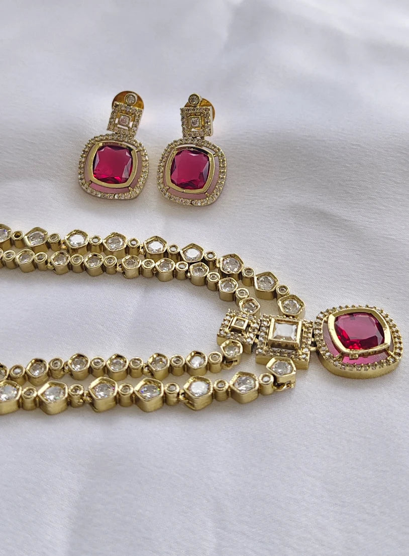 Gold necklace and earrings with red gemstones on a white background